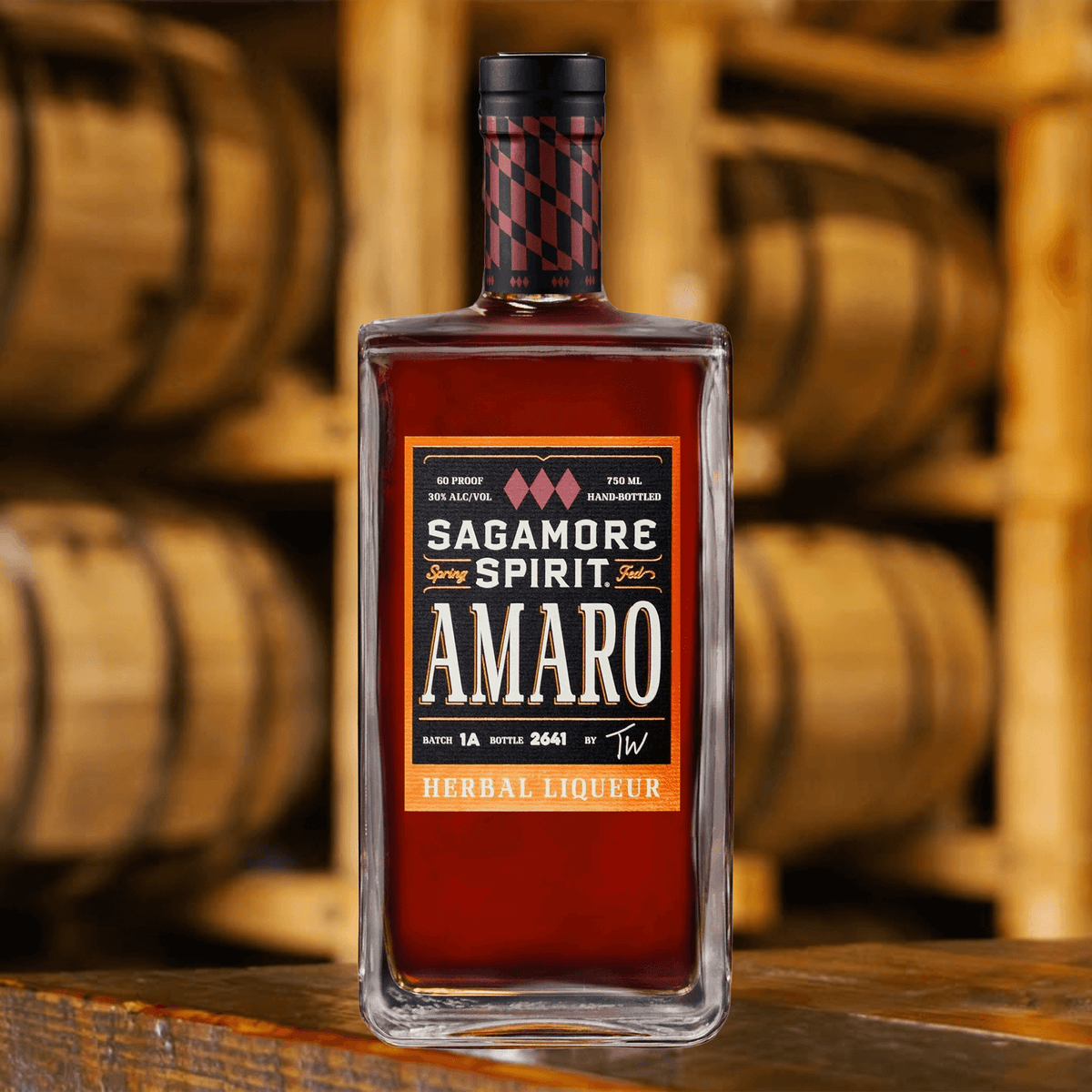 Sagamore Spirit Amaro Herbal Liqueur bottle with a rich amber color and wood barrels in the background.