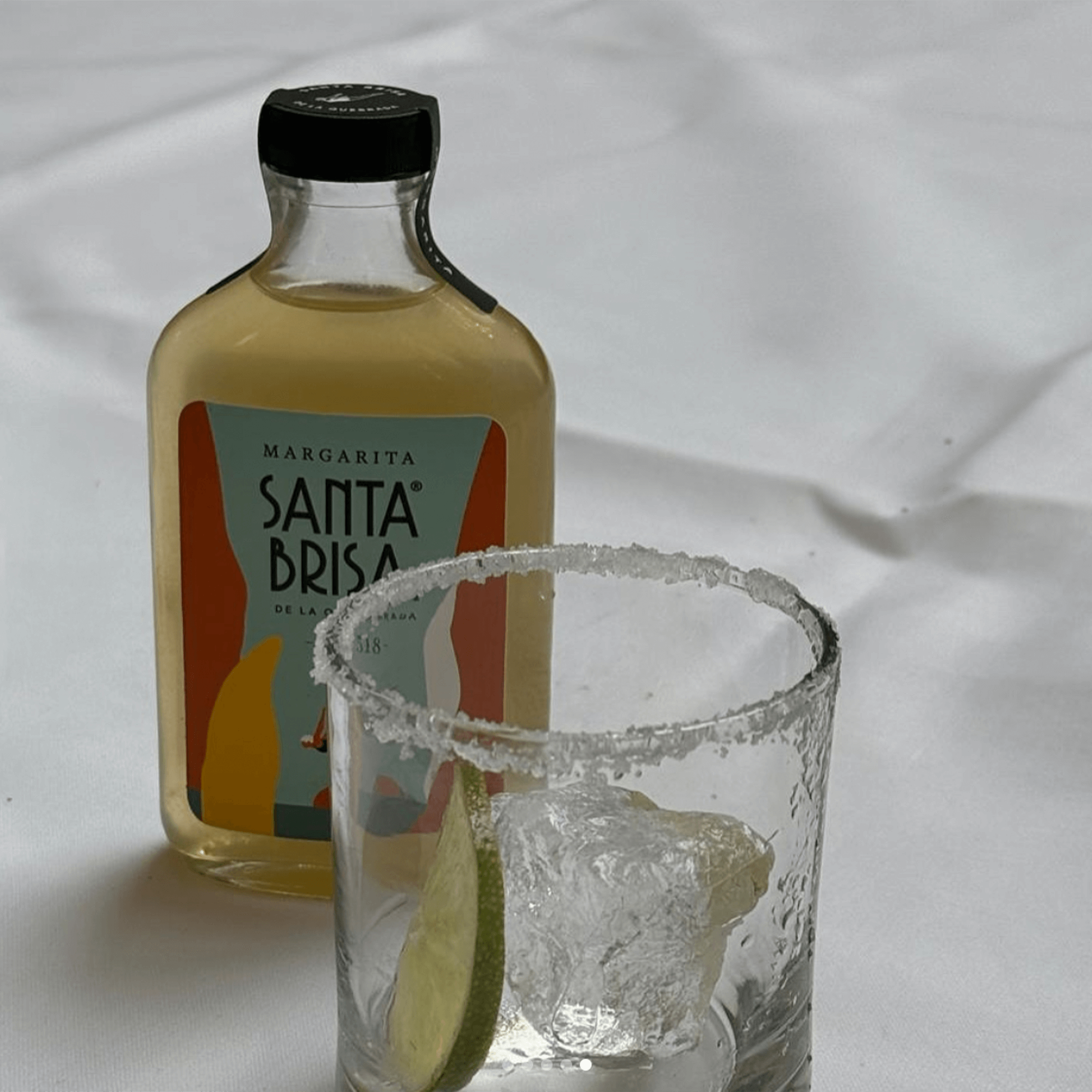 Santa Brisa Margarita cocktail bottle beside a glass with ice and lime slice, showcasing premium Mexican ingredients.