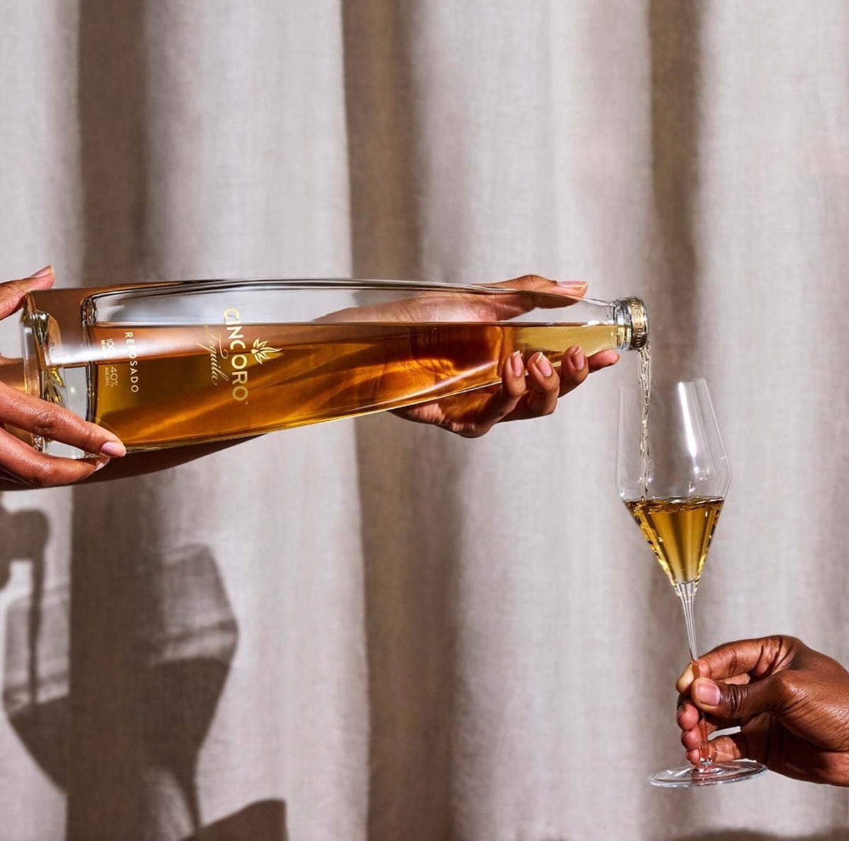 Pouring Cincoro Reposado Tequila into a glass, showcasing its smooth golden color and rich aromas.