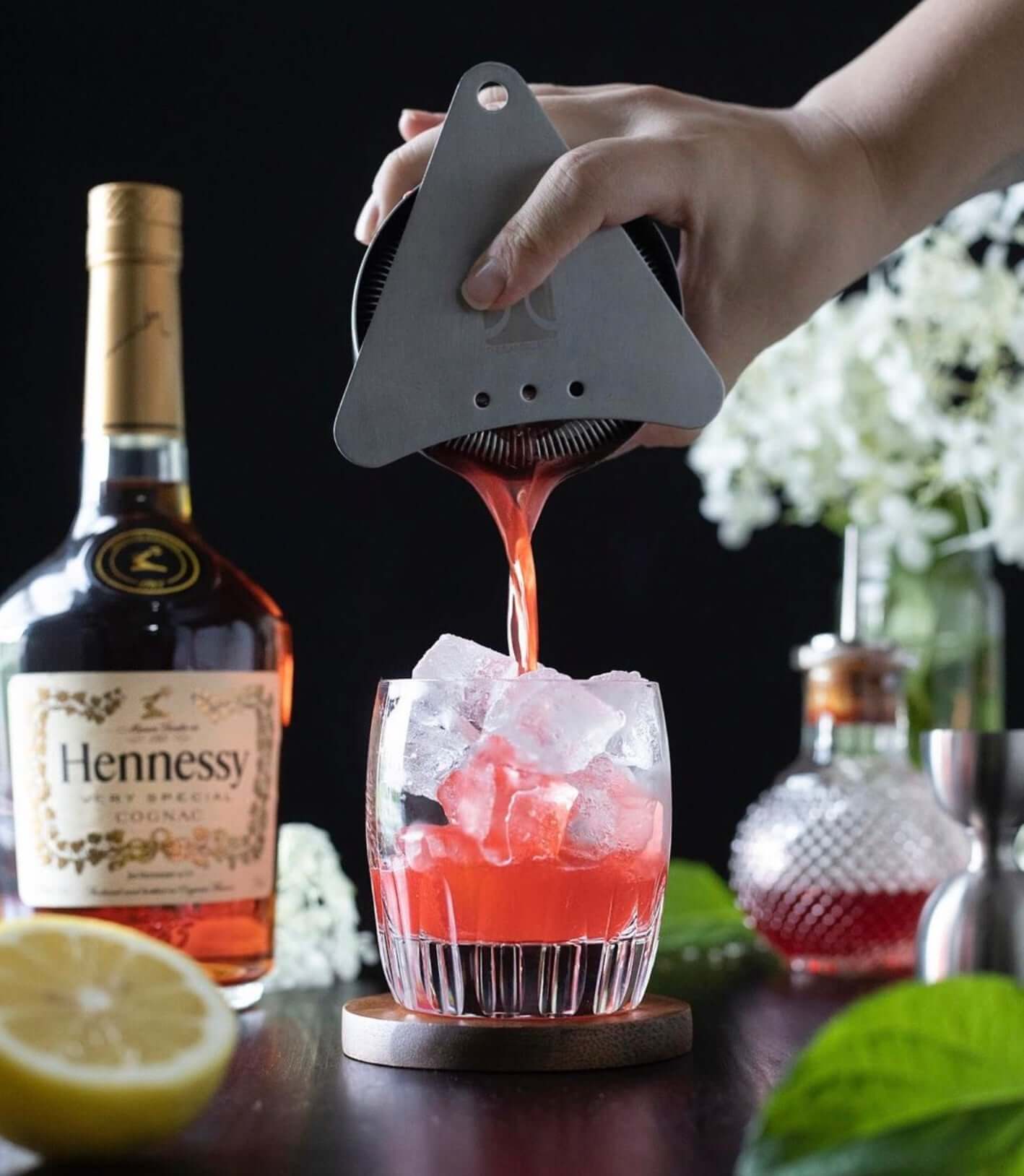 Hand pouring a vibrant cocktail made with Hennessy Very Special V.S Cognac over ice in a glass.