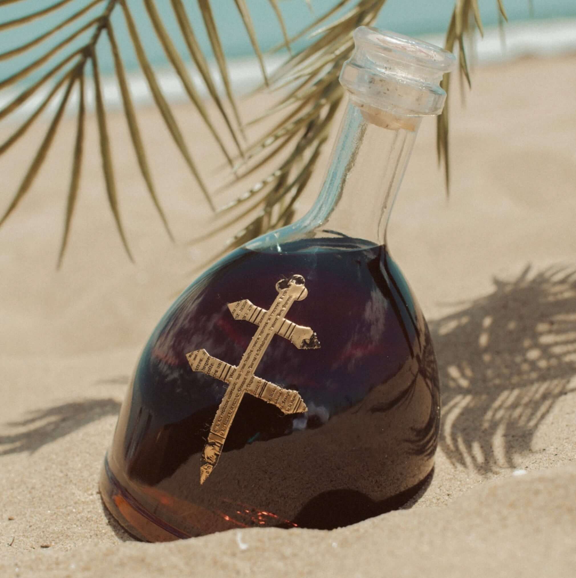 D'ussè VSOP 375ml bottle resting on sandy beach with palm leaves in the background.