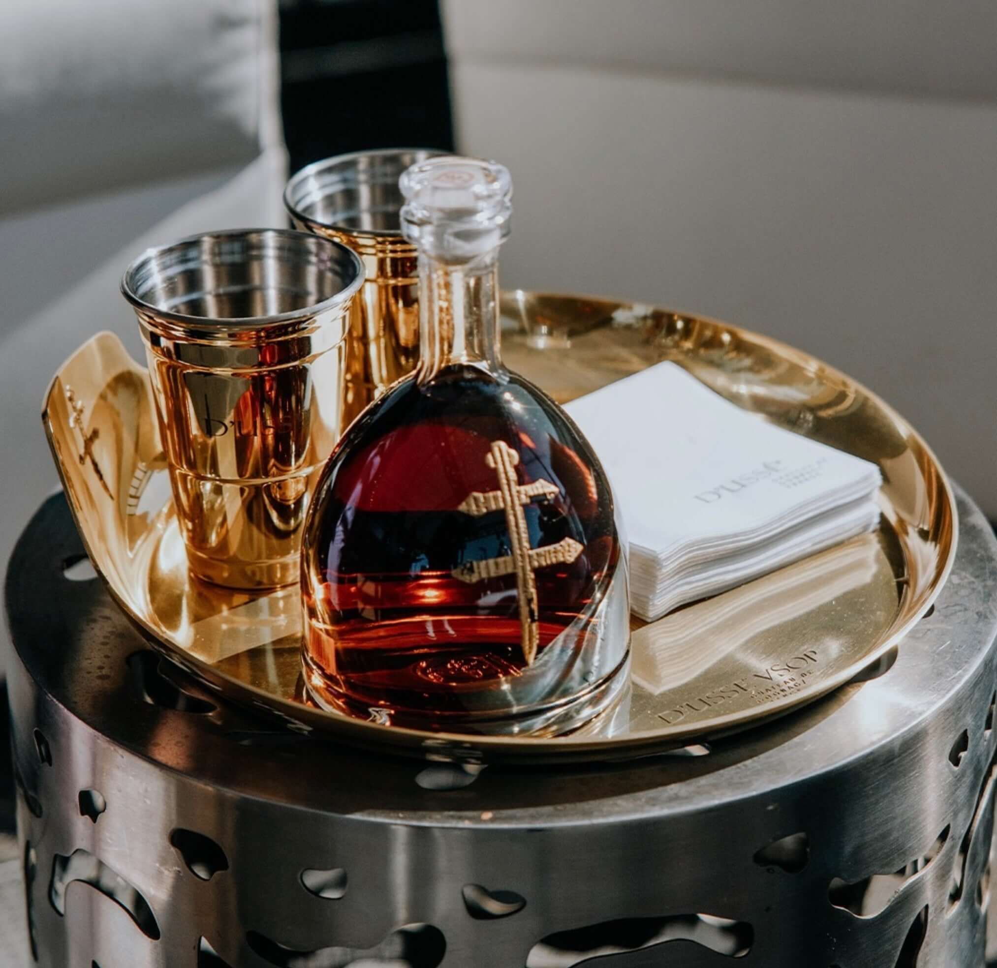 Elegant D'USSÉ VSOP Cognac in a glass decanter with gold cups and napkins on a stylish tray.