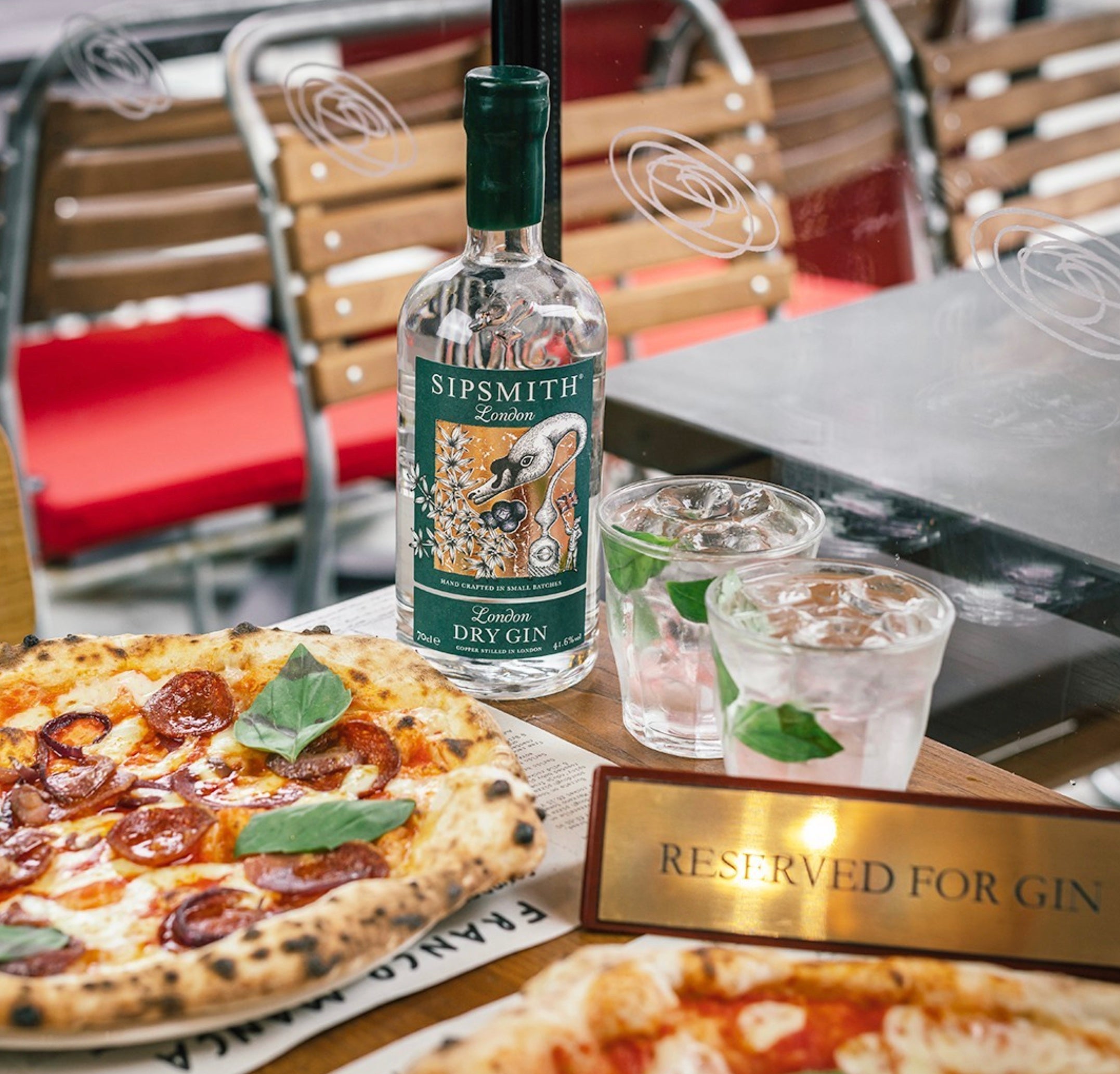 Sipsmith London Dry Gin bottle with two gin drinks and pizza on a table at a restaurant.