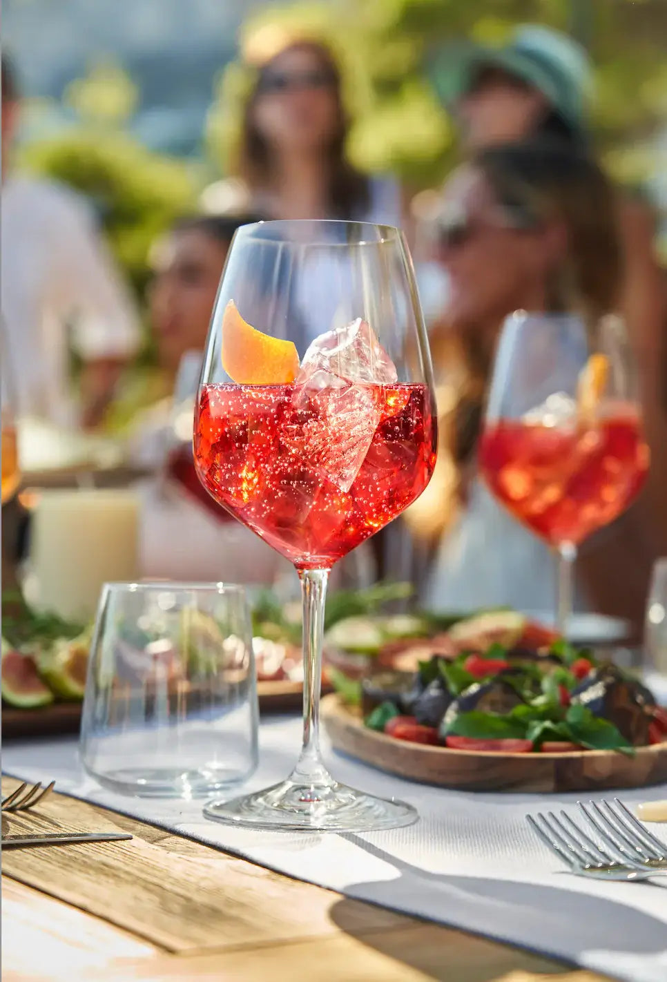 Refreshing Delola Bella Berry Spritz cocktail garnished with fruit, served at a vibrant outdoor gathering.