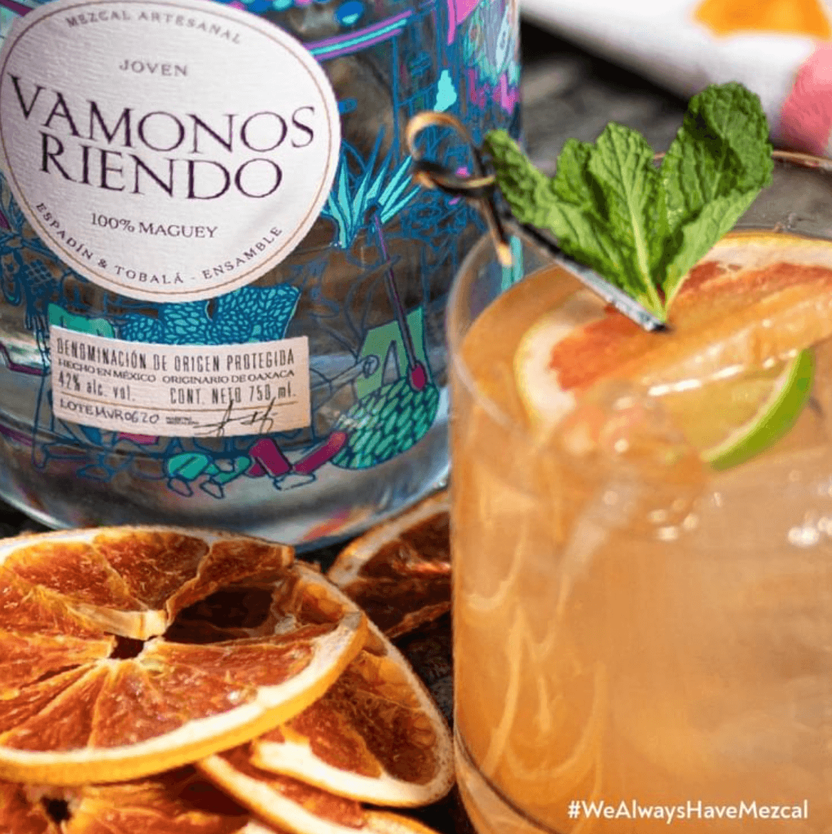 Vamonos Riendo Joven Mezcal bottle beside a cocktail garnished with mint and orange slices, showcasing artisanal craftsmanship.
