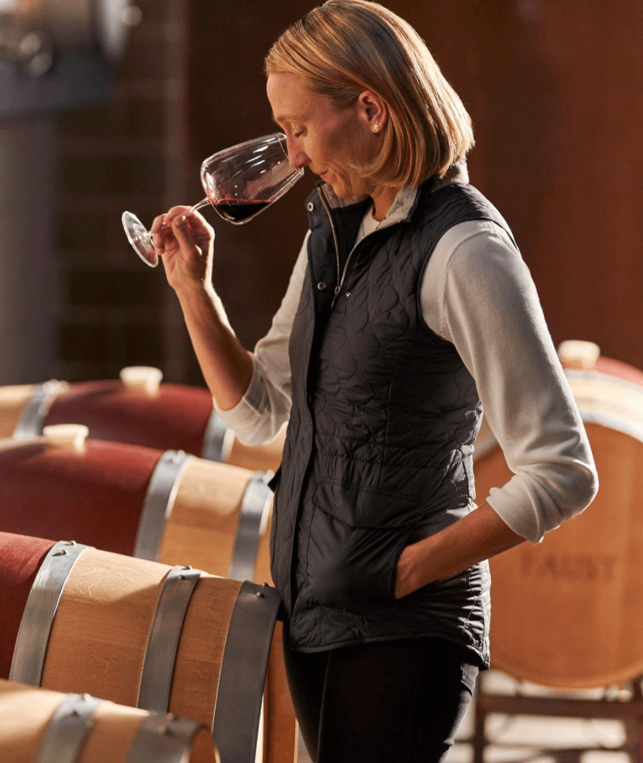 Woman savoring wine in a winery with oak barrels, showcasing Napa Valley's Faust Cabernet Sauvignon.