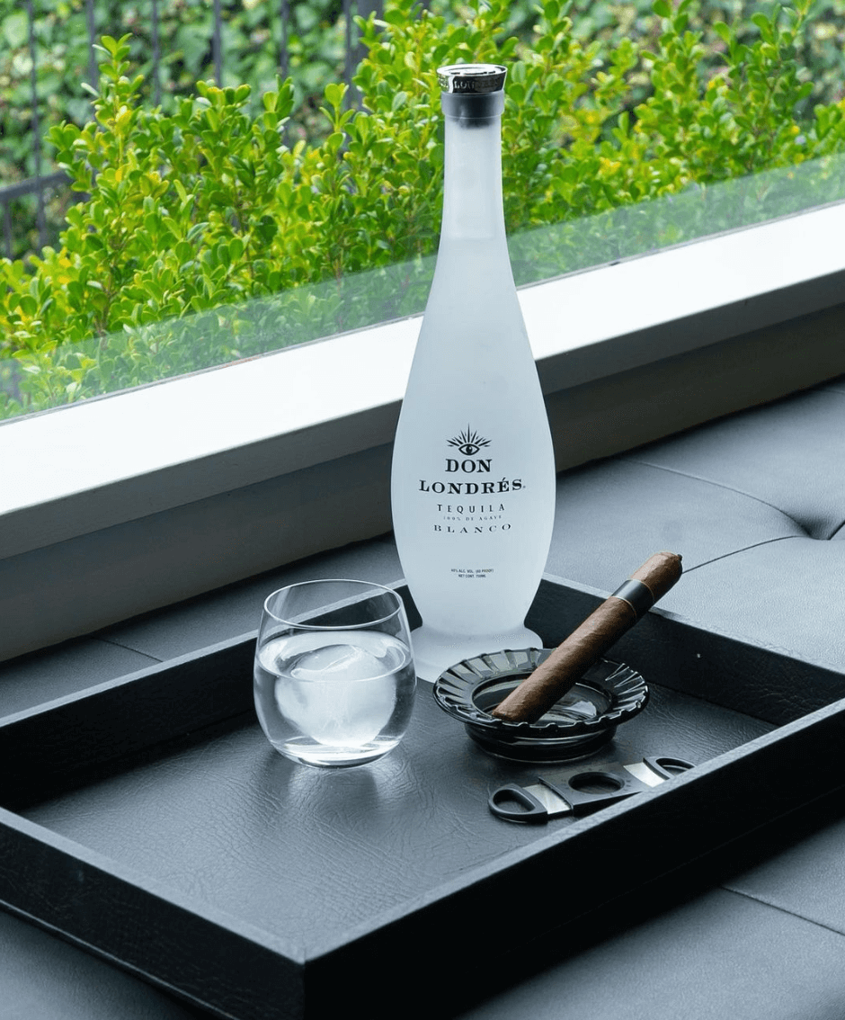 Elegant Don Londrés Blanco Tequila bottle with a glass and cigar on a stylish tray by the window.