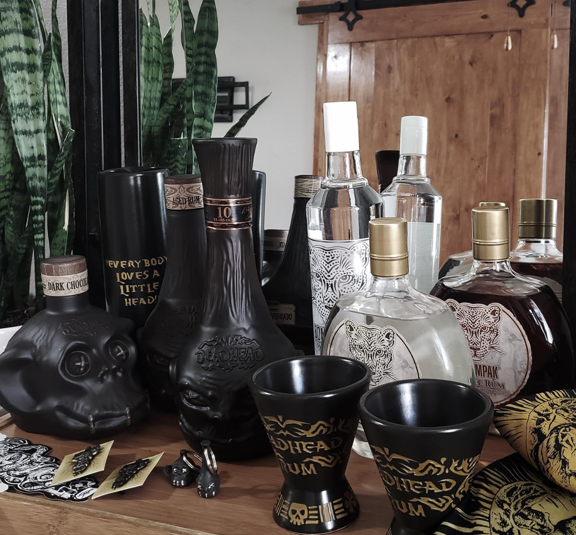 Display of Deadhead Dark Chocolate Monkey Head rum bottles and shot glasses on a wooden table.