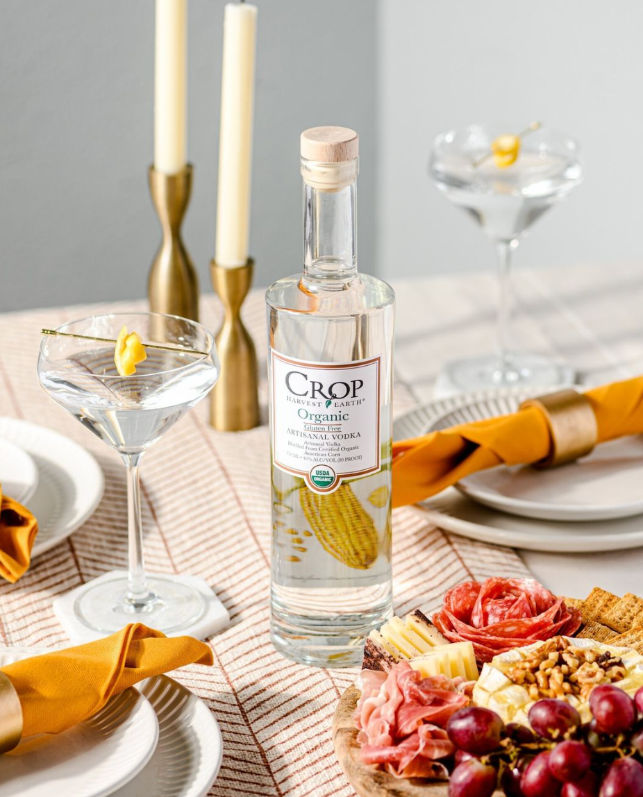 Bottle of Crop Organic Vodka displayed with cocktails and a charcuterie board, emphasizing organic farming benefits.
