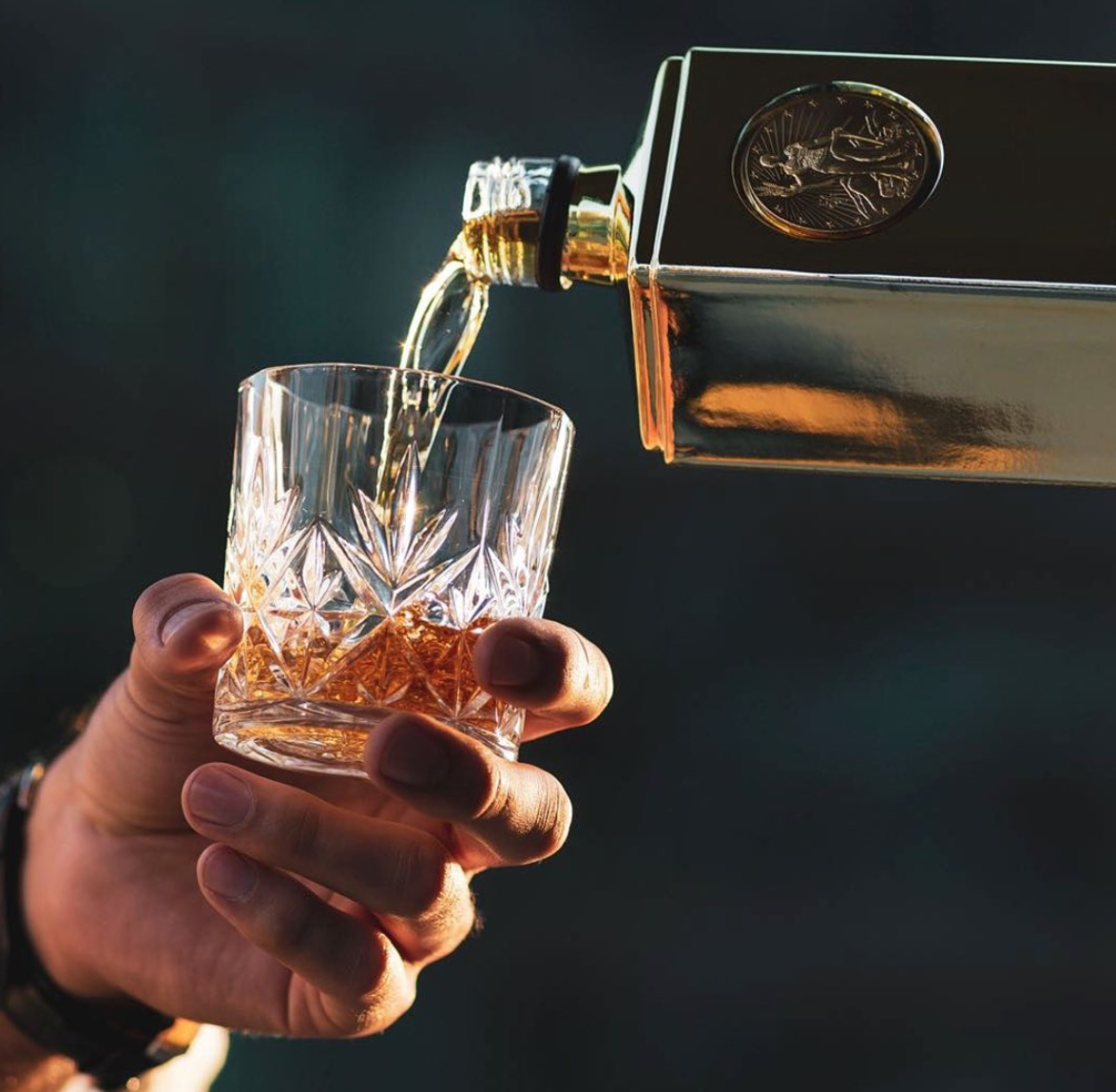 Pouring Gold Bar Original Premium Blended Whiskey into a crystal glass, showcasing its rich amber color and smooth texture.