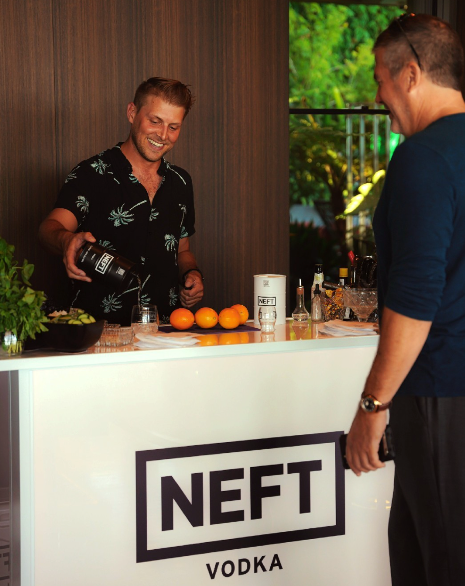 Bartender serving NEFT Black Barrel Vodka at a stylish bar with fresh ingredients and decorations.