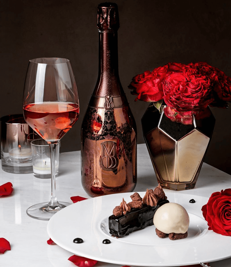 Luxury Mod Sélection Reserve Champagne bottle with dessert and roses, elegant dining setup.