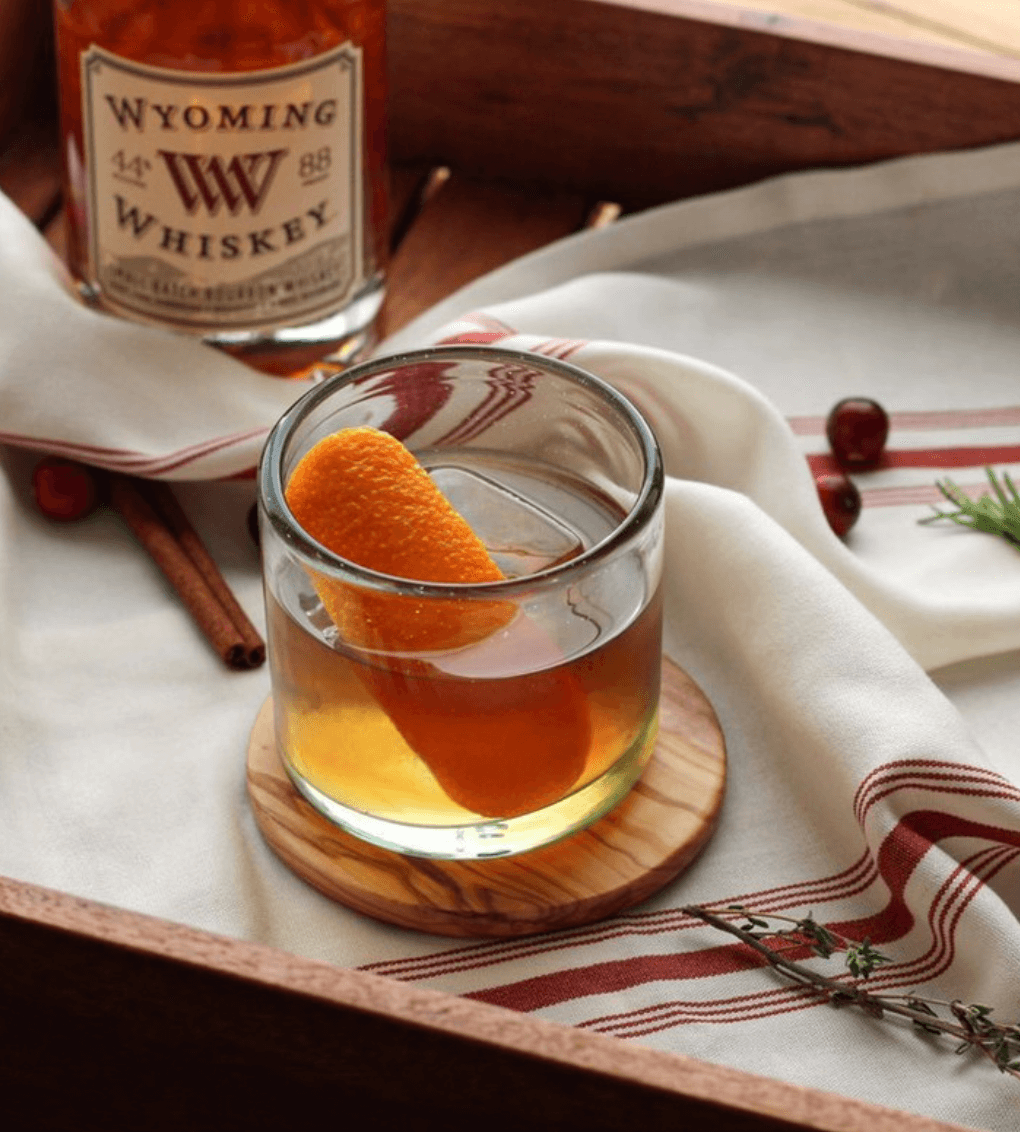 Glass of Wyoming Small Batch Bourbon Whiskey with an orange twist on a wooden coaster.