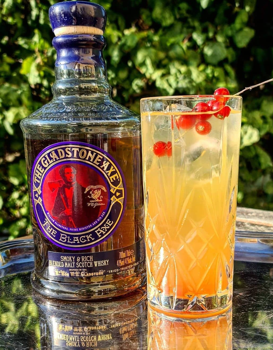 Bottle of Gladstone Axe Black Axe Scotch beside a refreshing cocktail garnished with red currants.