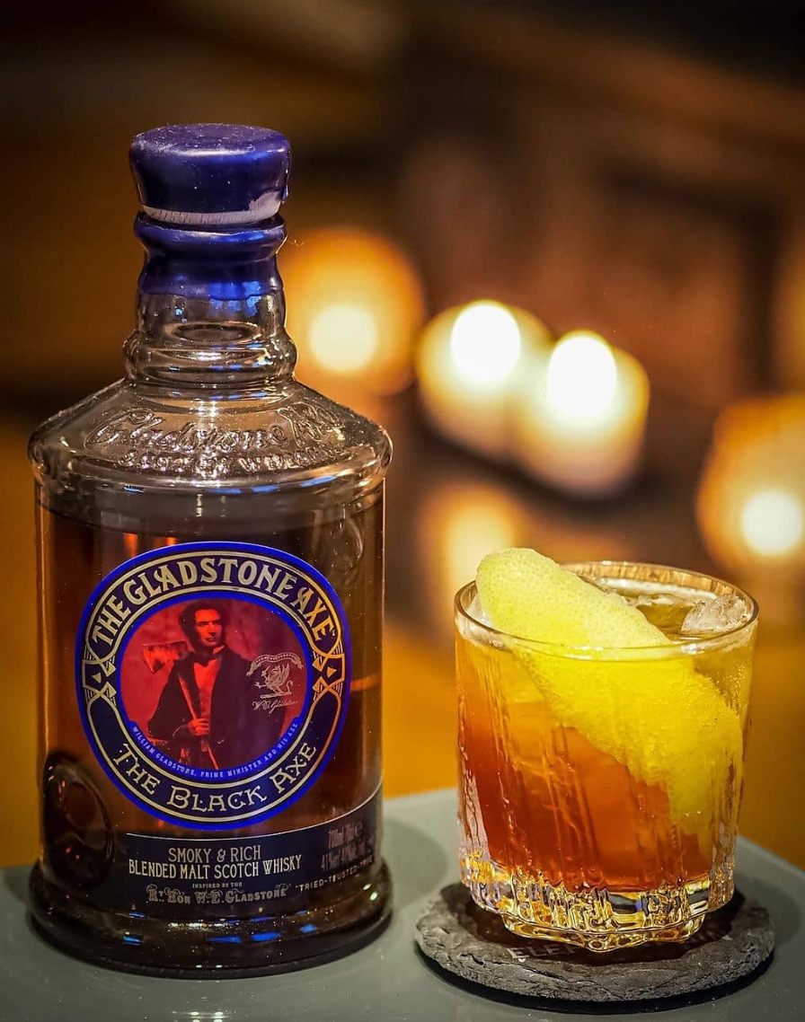 The Gladstone Axe The Black Axe Scotch bottle next to a glass with a smoky drink garnish.