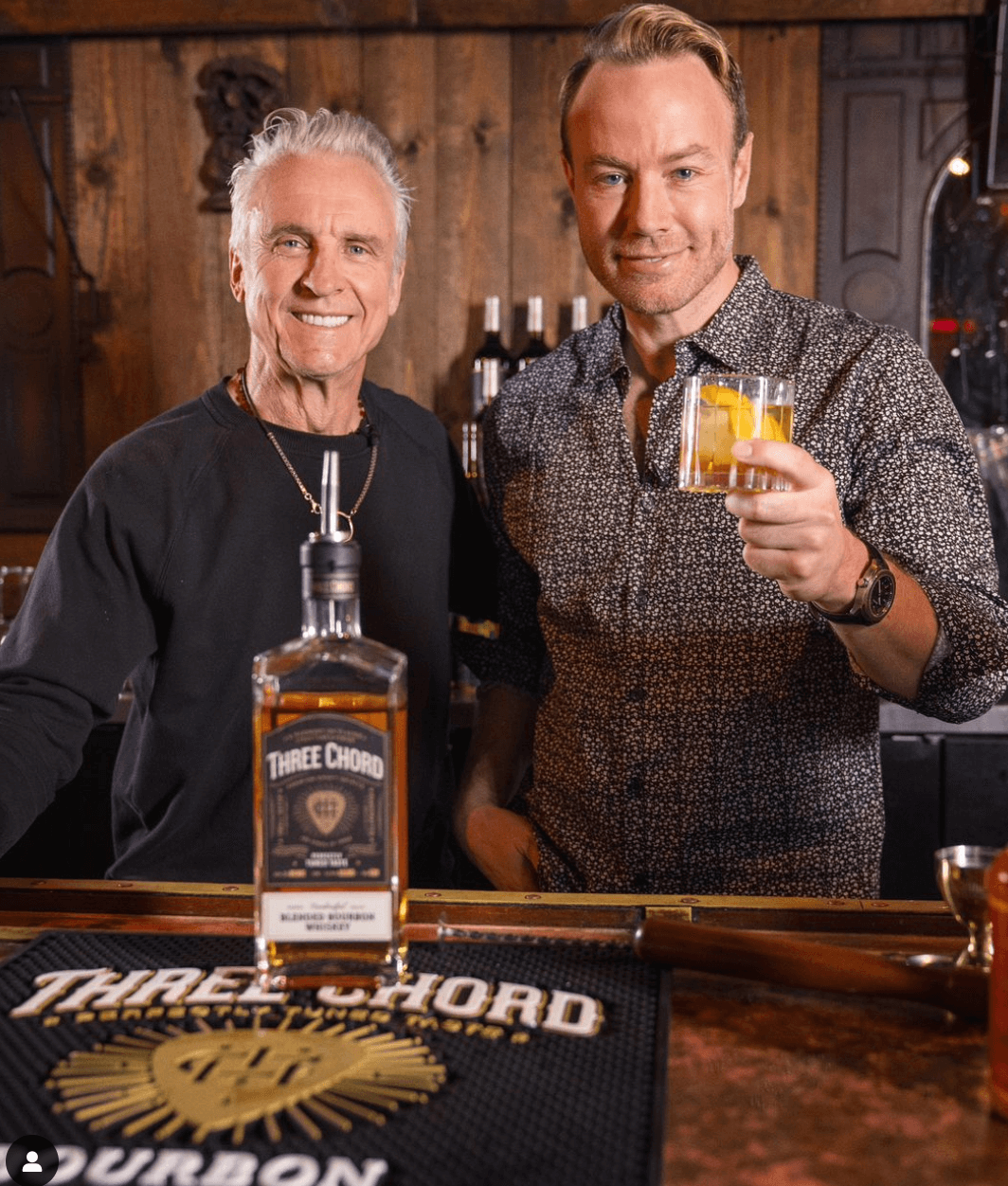 Two men enjoying Three Chord Small Batch Blended Bourbon at a bar, showcasing the bottle and cocktails.
