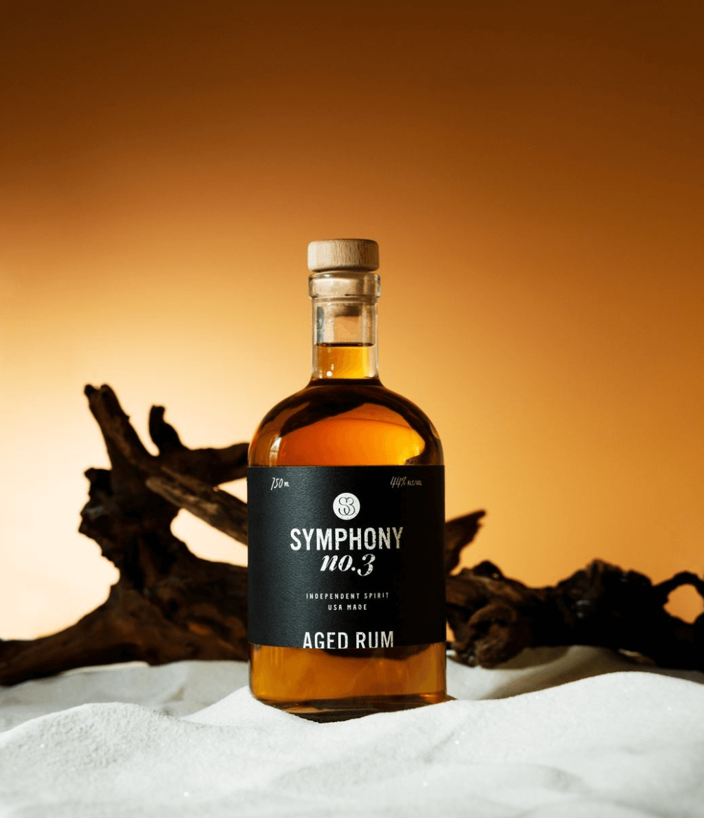 Symphony No. 3 Aged Rum bottle on sandy surface, showcasing amber color and elegant design.