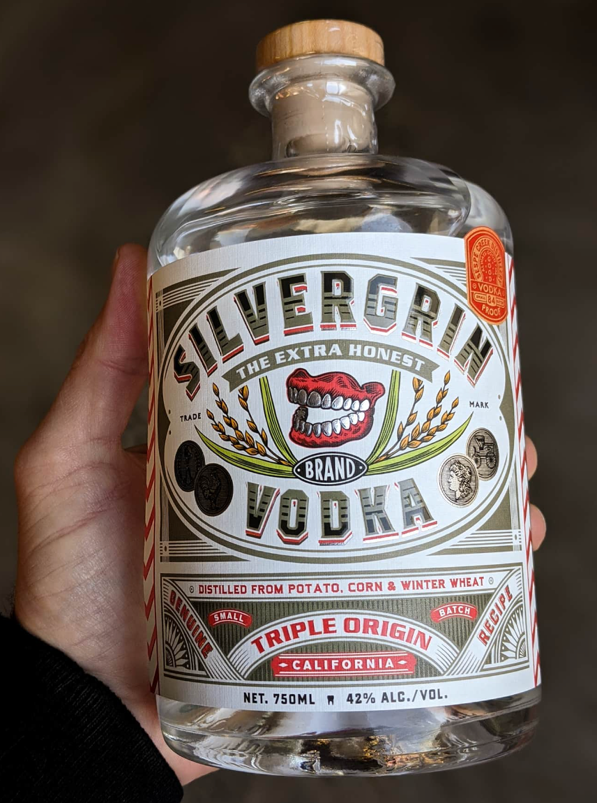 Hand holding a bottle of Silvergrin Triple Origin Vodka, showcasing its label and distinctive design.