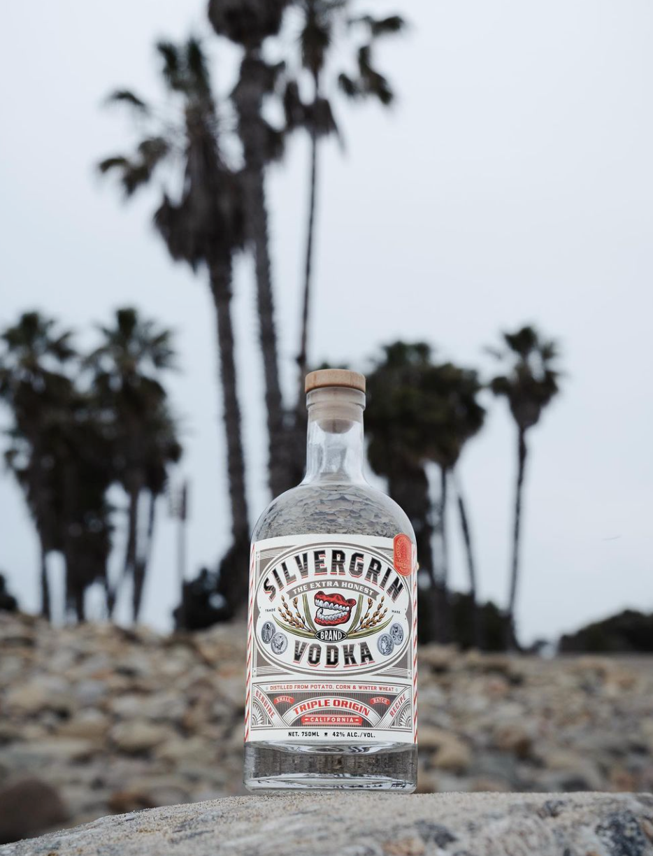 Bottle of Silvergrin Triple Origin Vodka with palm trees in the background, showcasing premium quality vodka from Montana.
