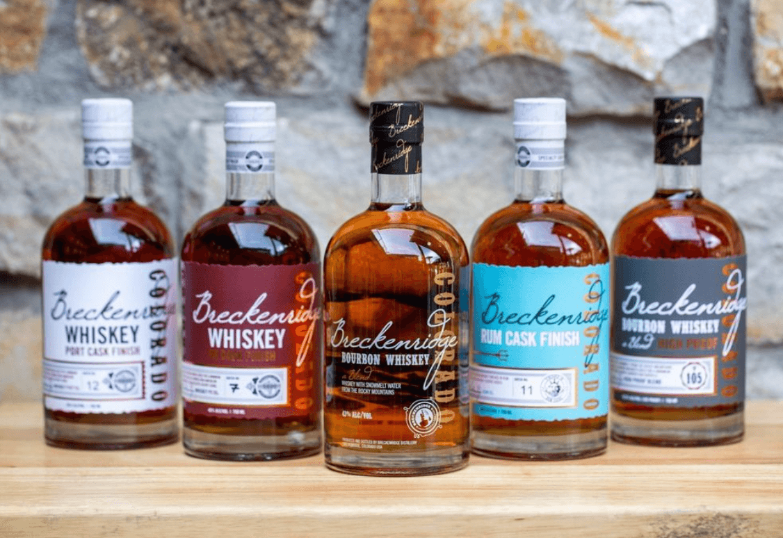 Five bottles of Breckenridge Bourbon Whiskey and other finishes displayed on a wooden surface against a stone background.