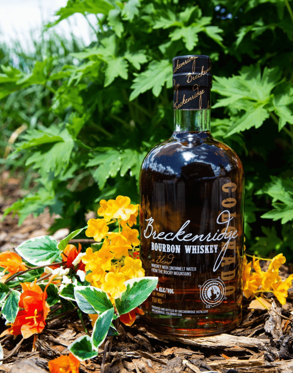 Breckenridge Bourbon Whiskey bottle surrounded by vibrant flowers and greenery, showcasing its rich amber color.