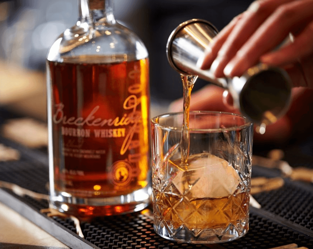 Pouring Breckenridge Bourbon Whiskey into a glass with a large ice cube, showcasing its rich amber color.