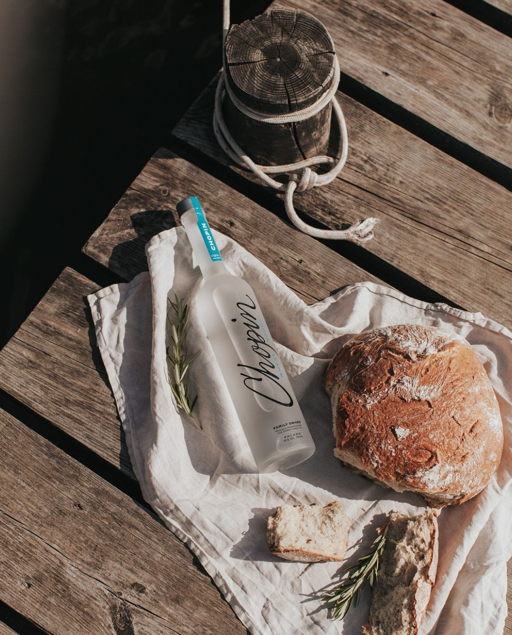 Chopin Wheat Vodka bottle beside fresh bread and herbs on a wooden table, perfect for summer cocktails.