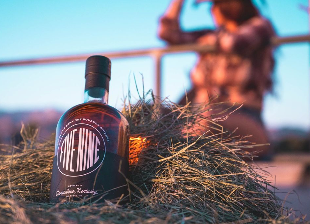 Five Nine Kentucky Straight Bourbon Whiskey bottle placed on hay with a sunset backdrop.
