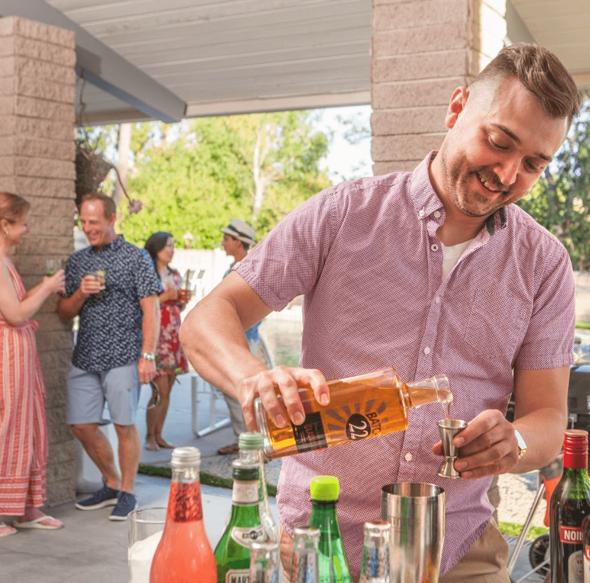 Man pouring Batch 22 New American Aquavit into a cocktail shaker at a lively outdoor gathering.