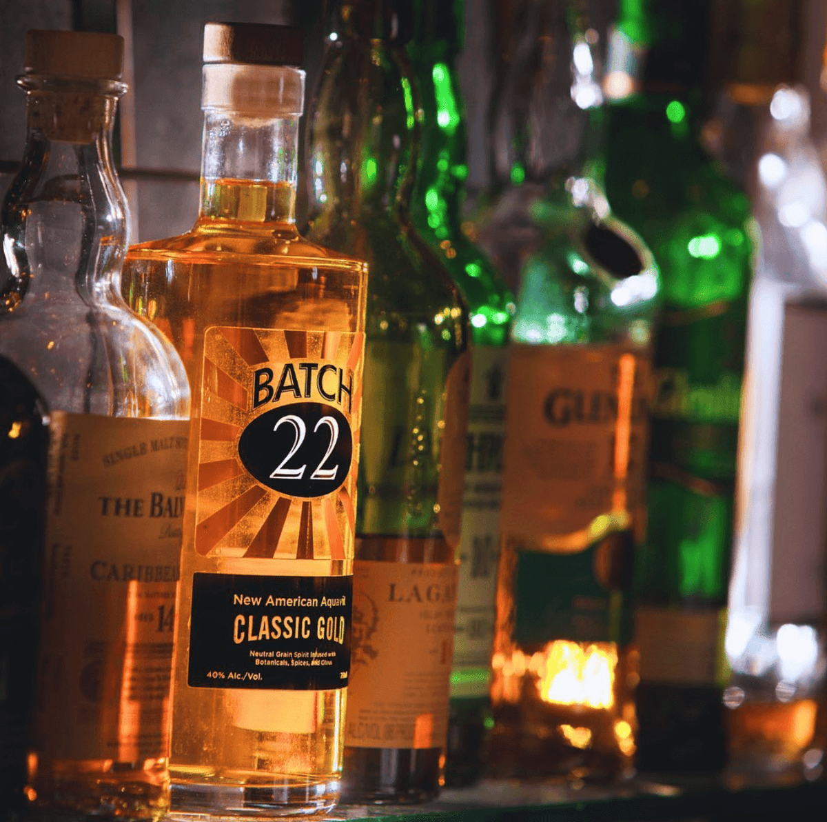 Batch 22 New American Aquavit Classic Gold bottle among a selection of liquor bottles, showcasing its unique golden hue.