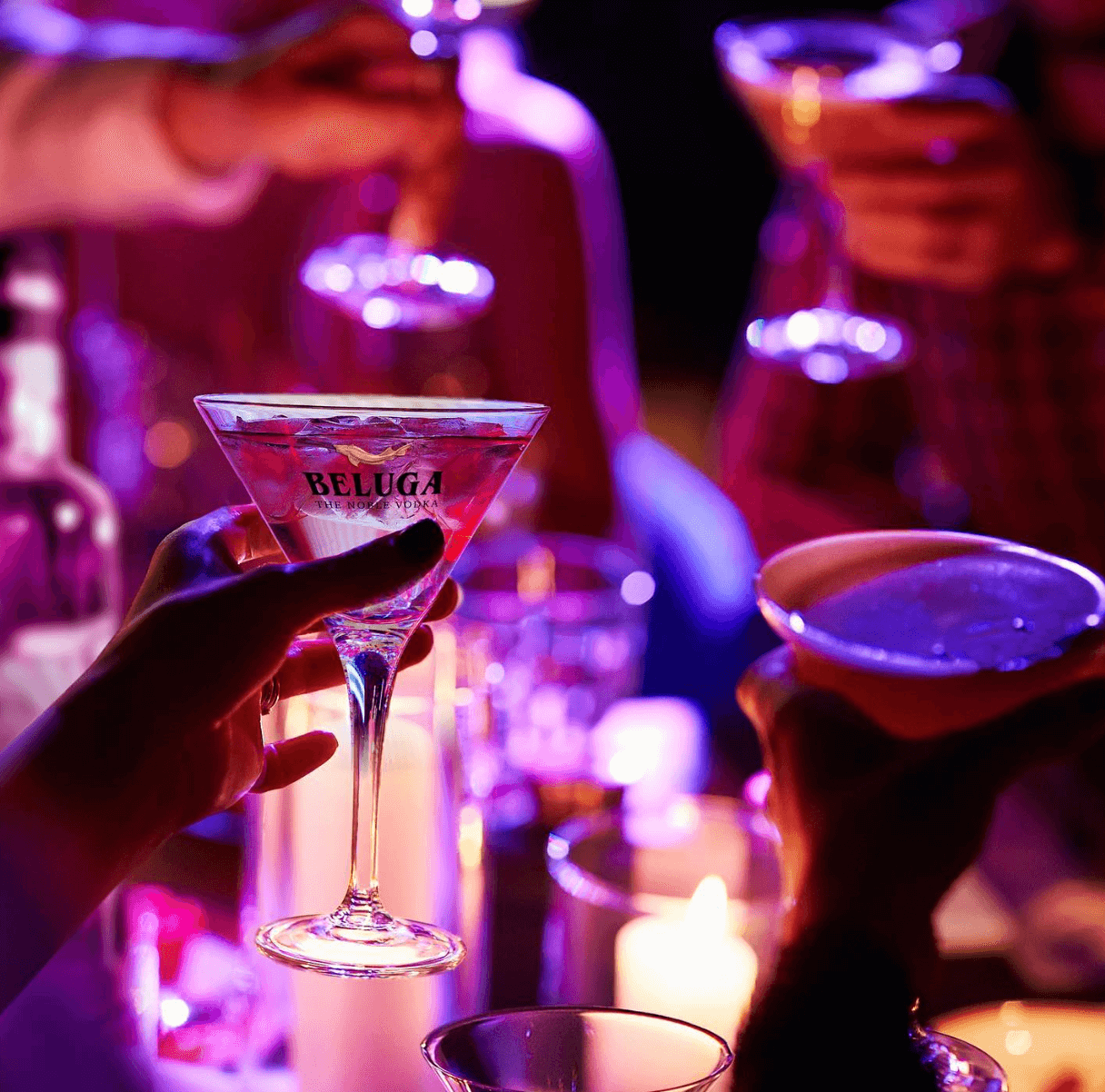 Group of friends toasting with Beluga Transatlantic Vodka cocktails in a lively ambiance with candles.