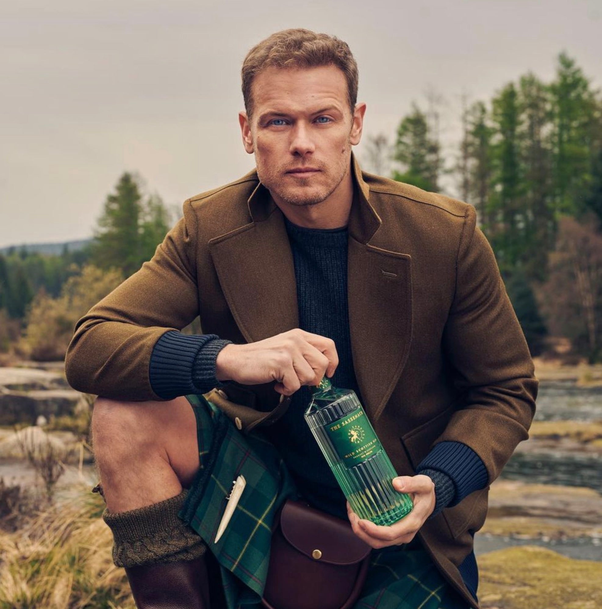 Man in a kilt holding Sassenach Wild Scottish Gin in a scenic Scottish landscape.