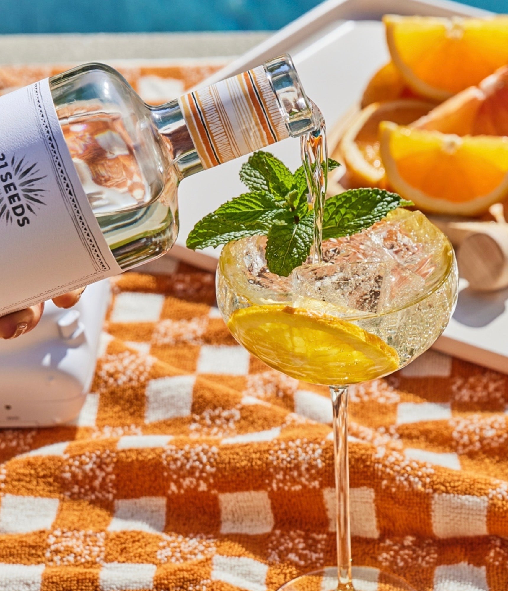 Pouring 21 Seeds Valencia Orange Tequila into a cocktail glass garnished with mint and orange on a sunny day.