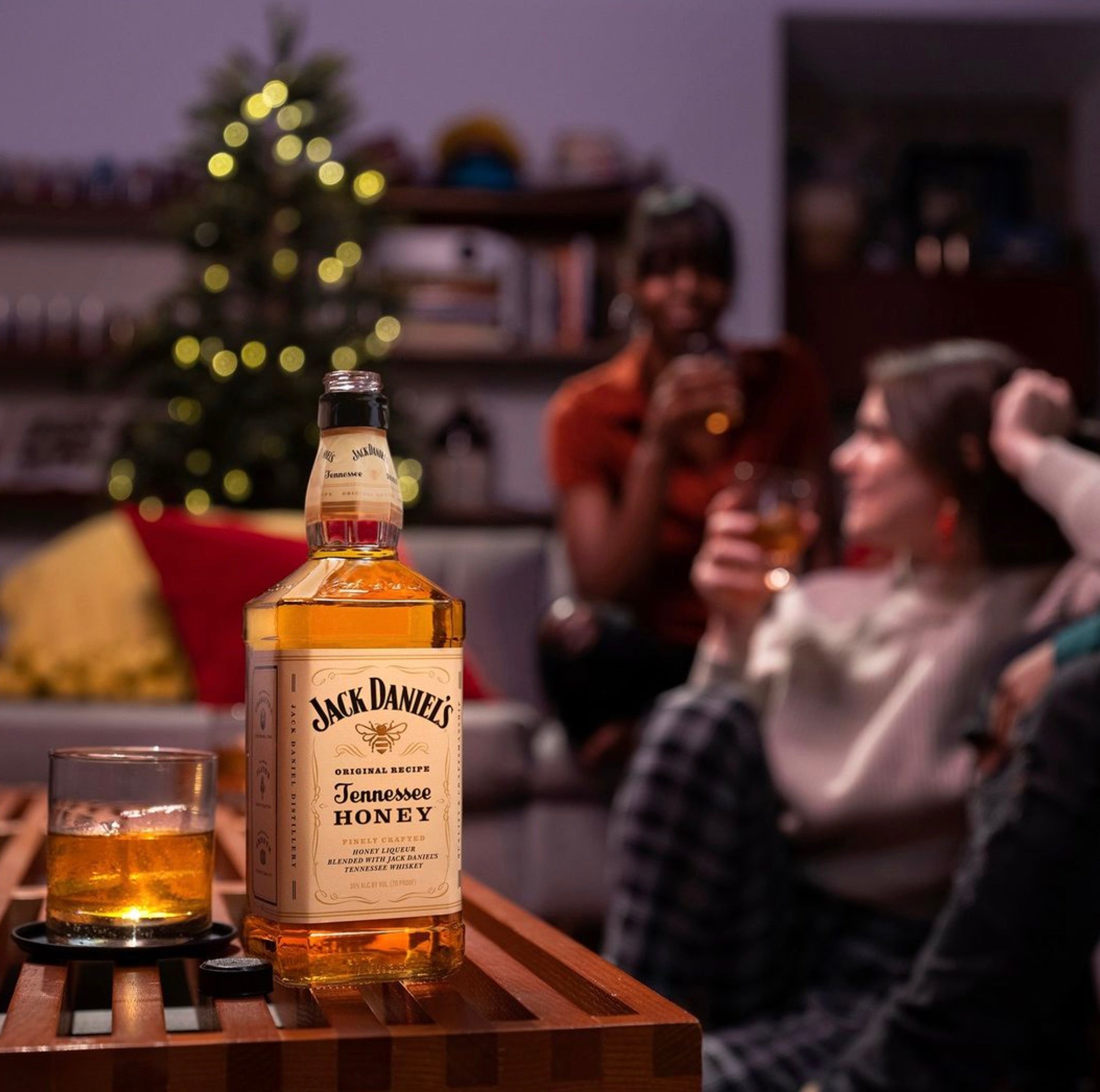 Jack Daniel's Tennessee Honey bottle on a table, with friends enjoying drinks in a festive living room.