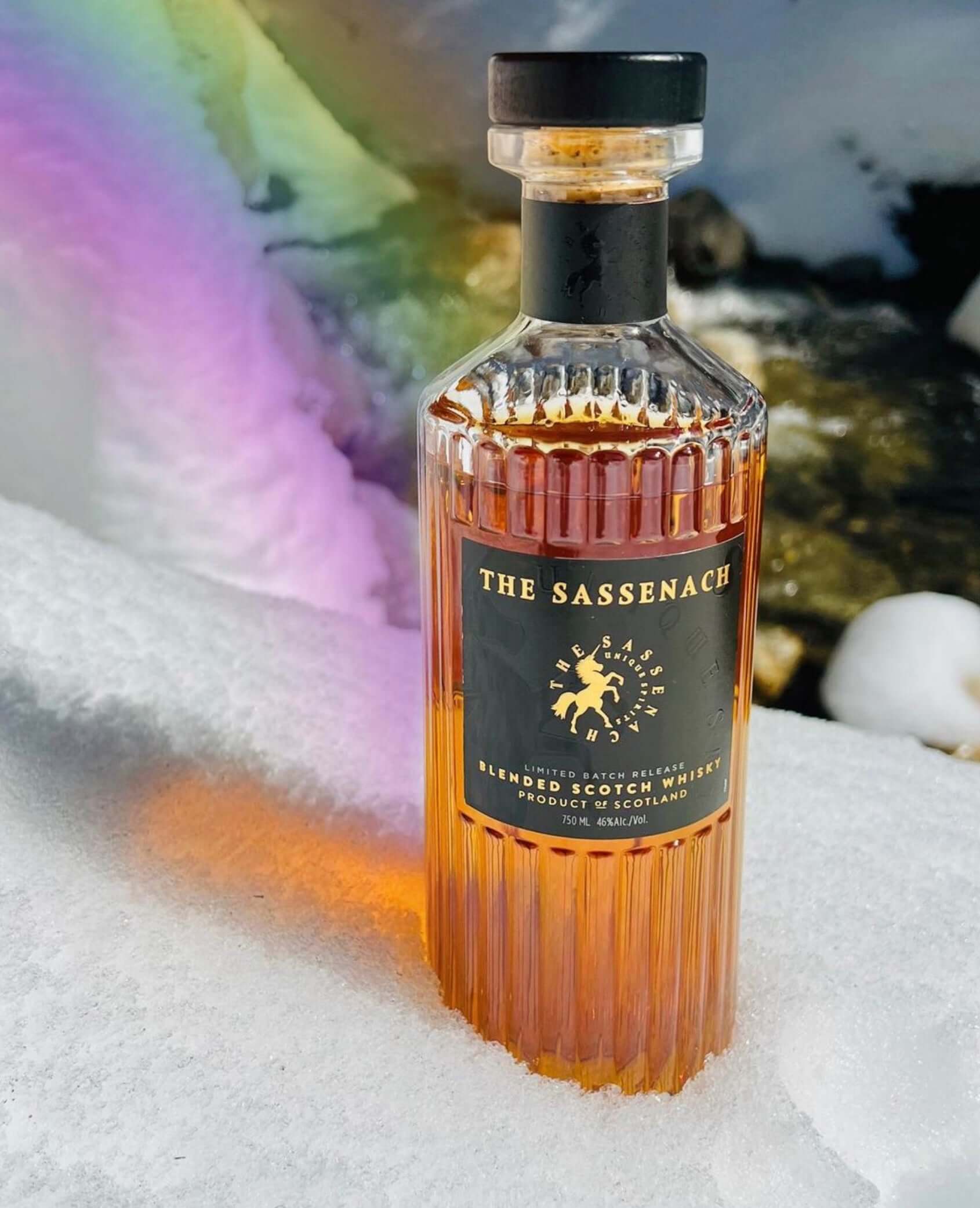 The Sassenach Blended Scotch Whisky bottle on snow with a colorful background, showcasing its rich amber color.