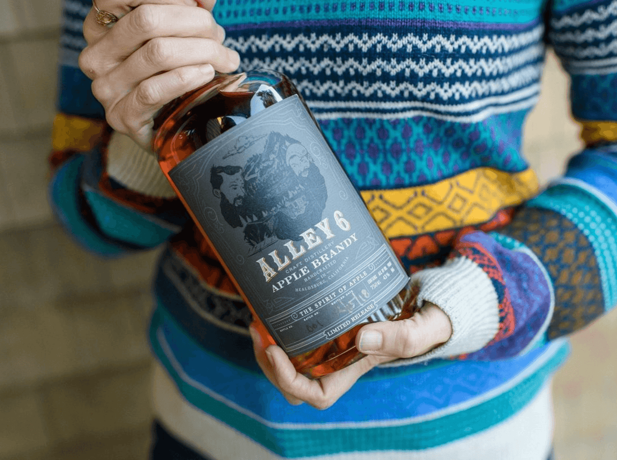 Person holding a bottle of Alley 6 Apple Brandy, showcasing its detailed label and warm colors.