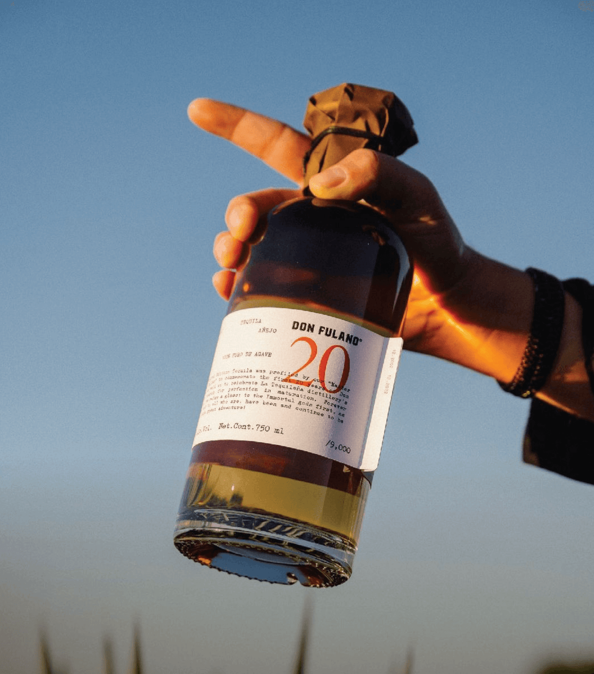 Don Fulano 20th Anniversary Añejo Tequila bottle held against a clear sky, showcasing limited edition label.