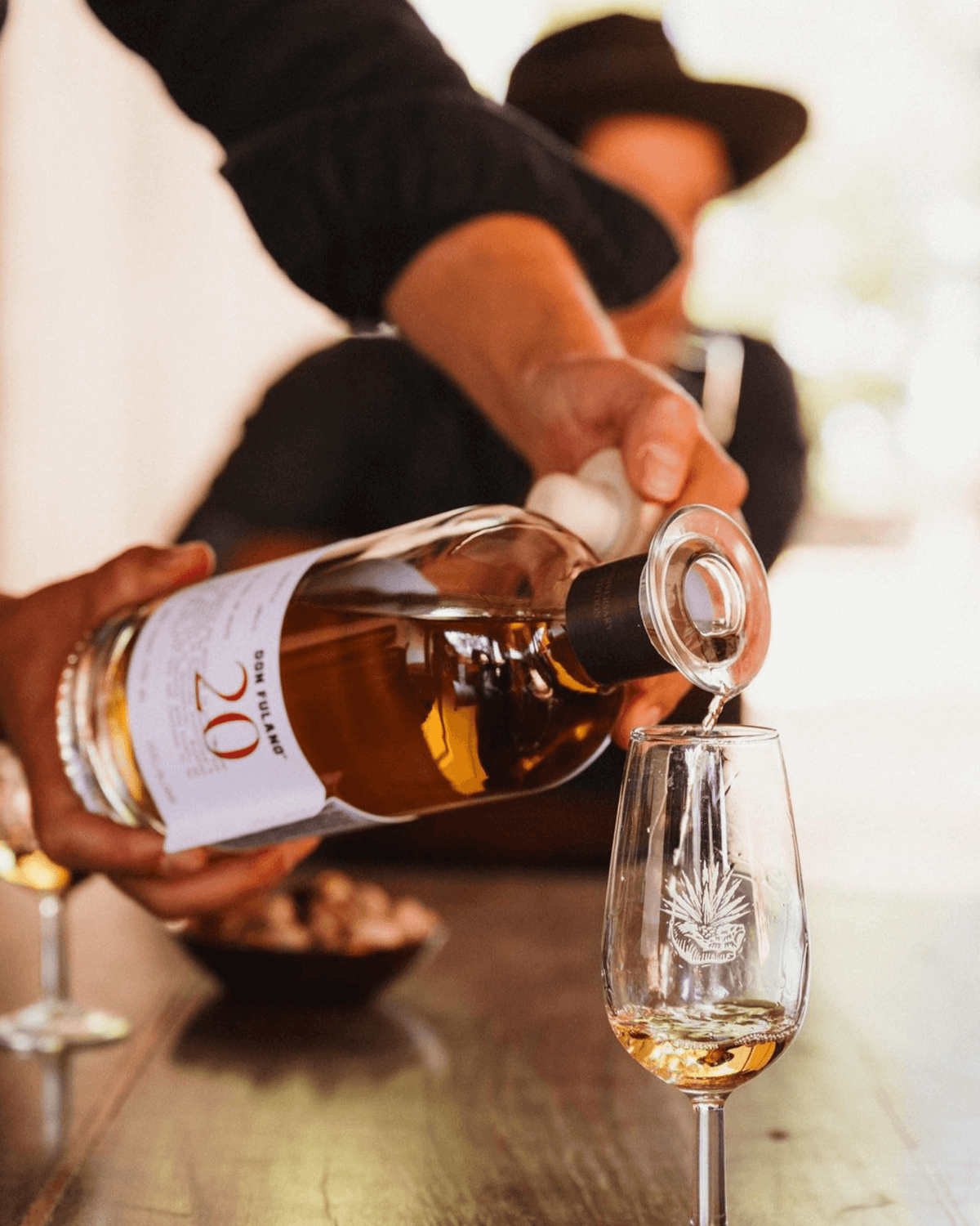 Pouring Don Fulano 20th Anniversary Añejo Tequila into a glass, showcasing the rich amber color and festive atmosphere.