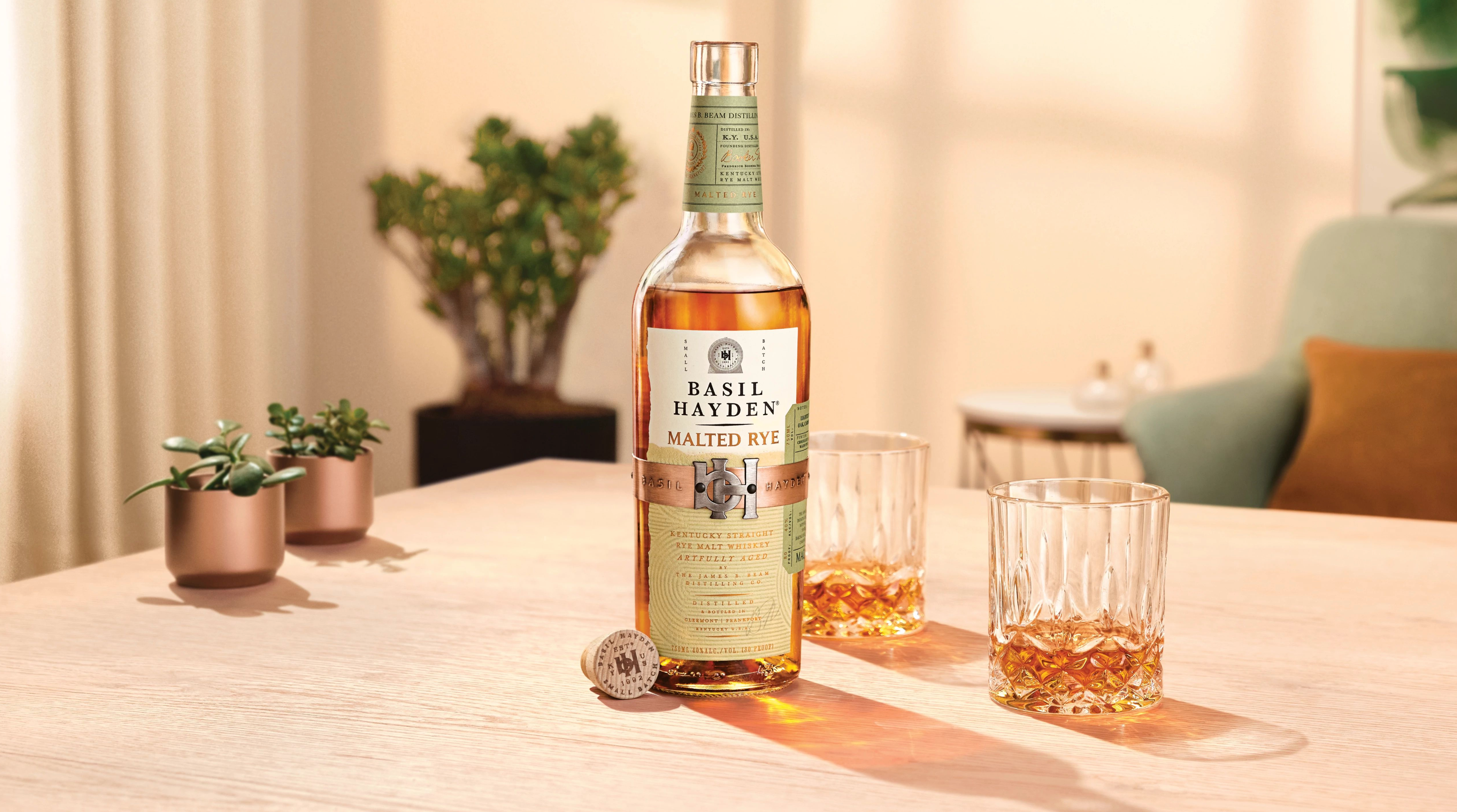 Basil Hayden Malted Rye whiskey bottle with two glasses on a wooden table, showcasing its unique malting process and softness.