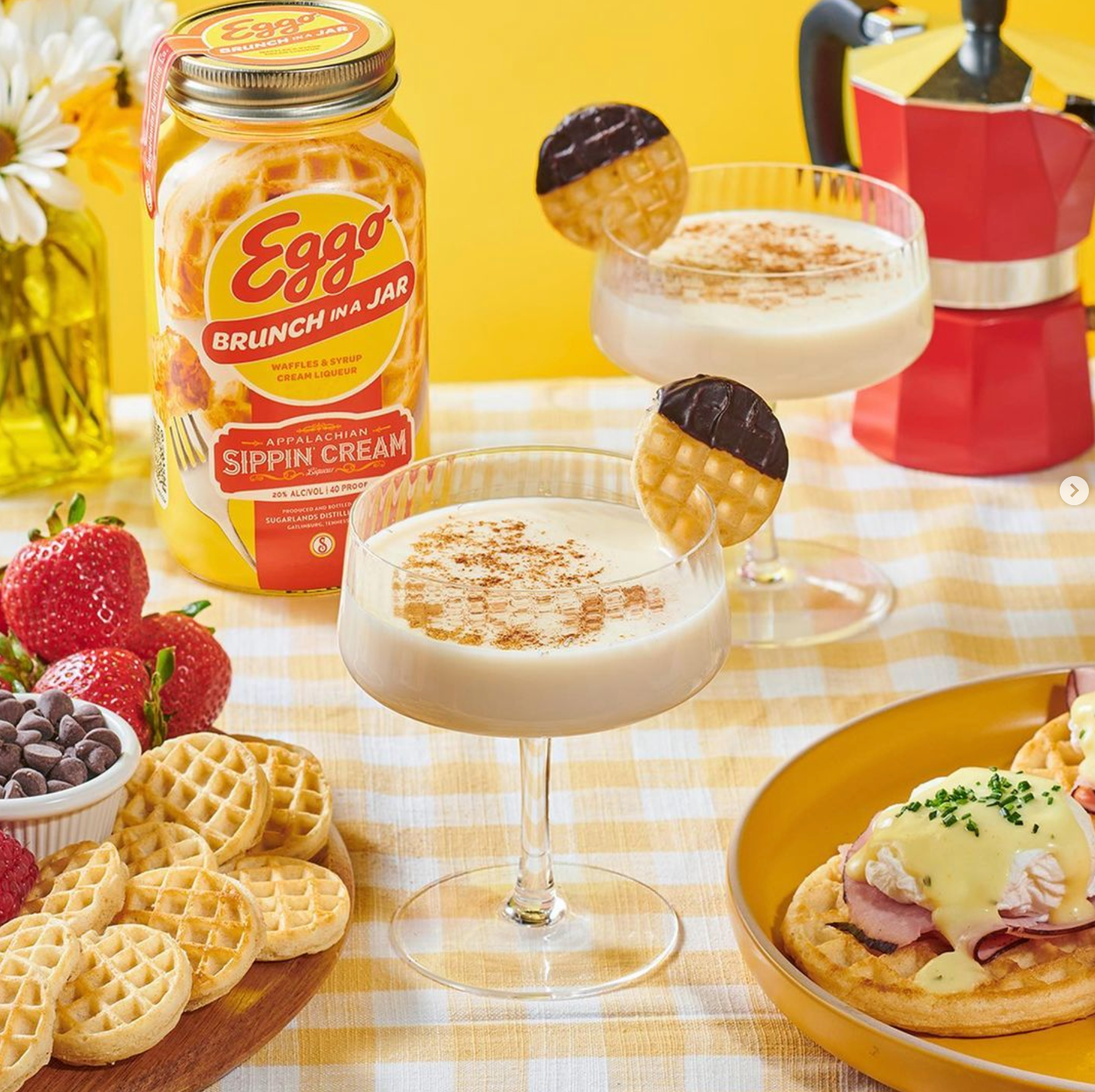 Two glasses of Eggo Nog Sippin' Cream with waffles and strawberries on a colorful brunch table.