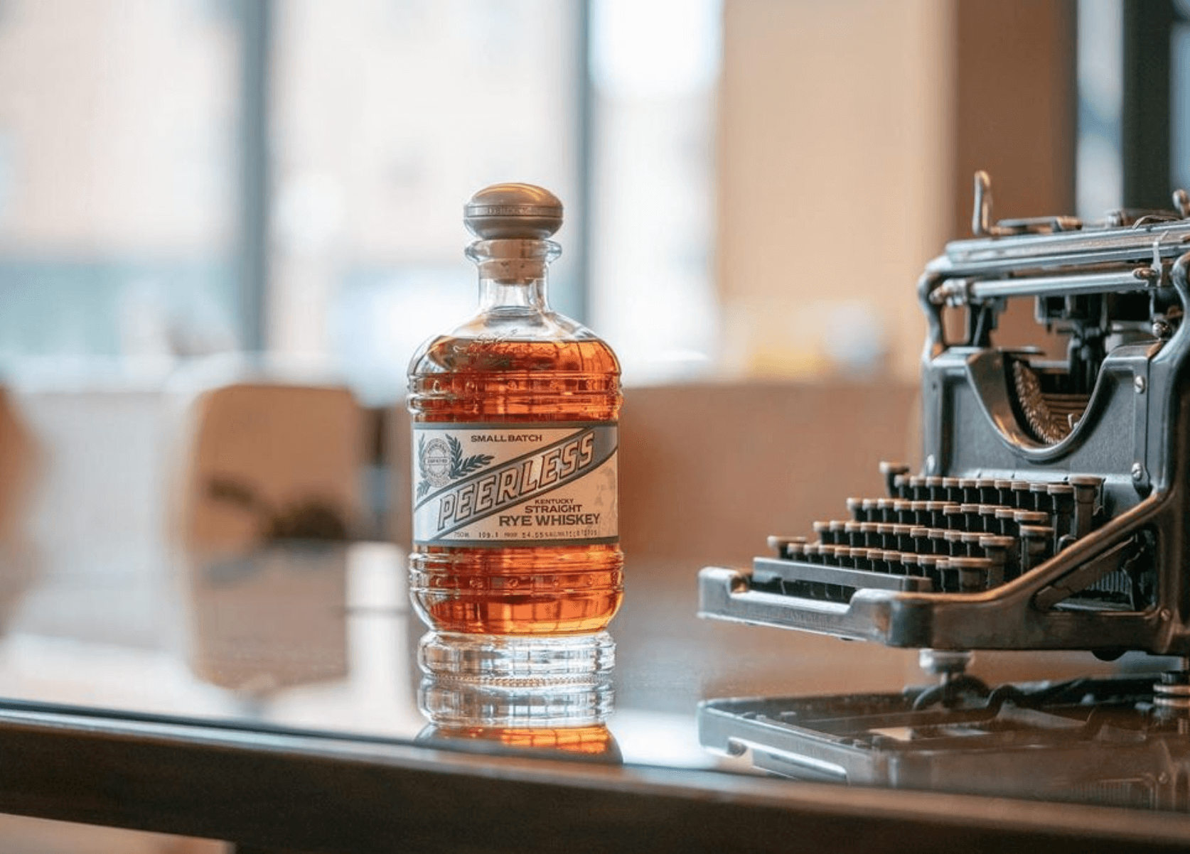 Bottle of Peerless Kentucky Straight Rye Whiskey on a table beside a vintage typewriter.