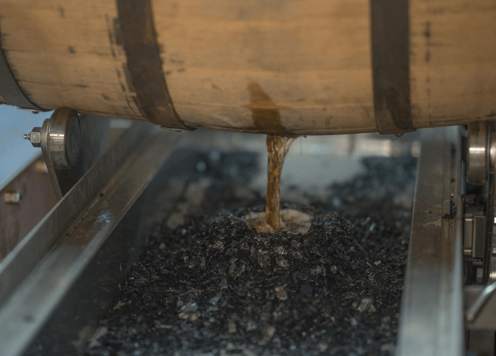 Barrel pouring Peerless Kentucky Straight Rye Whiskey into a collection tank, showcasing rich amber liquid.