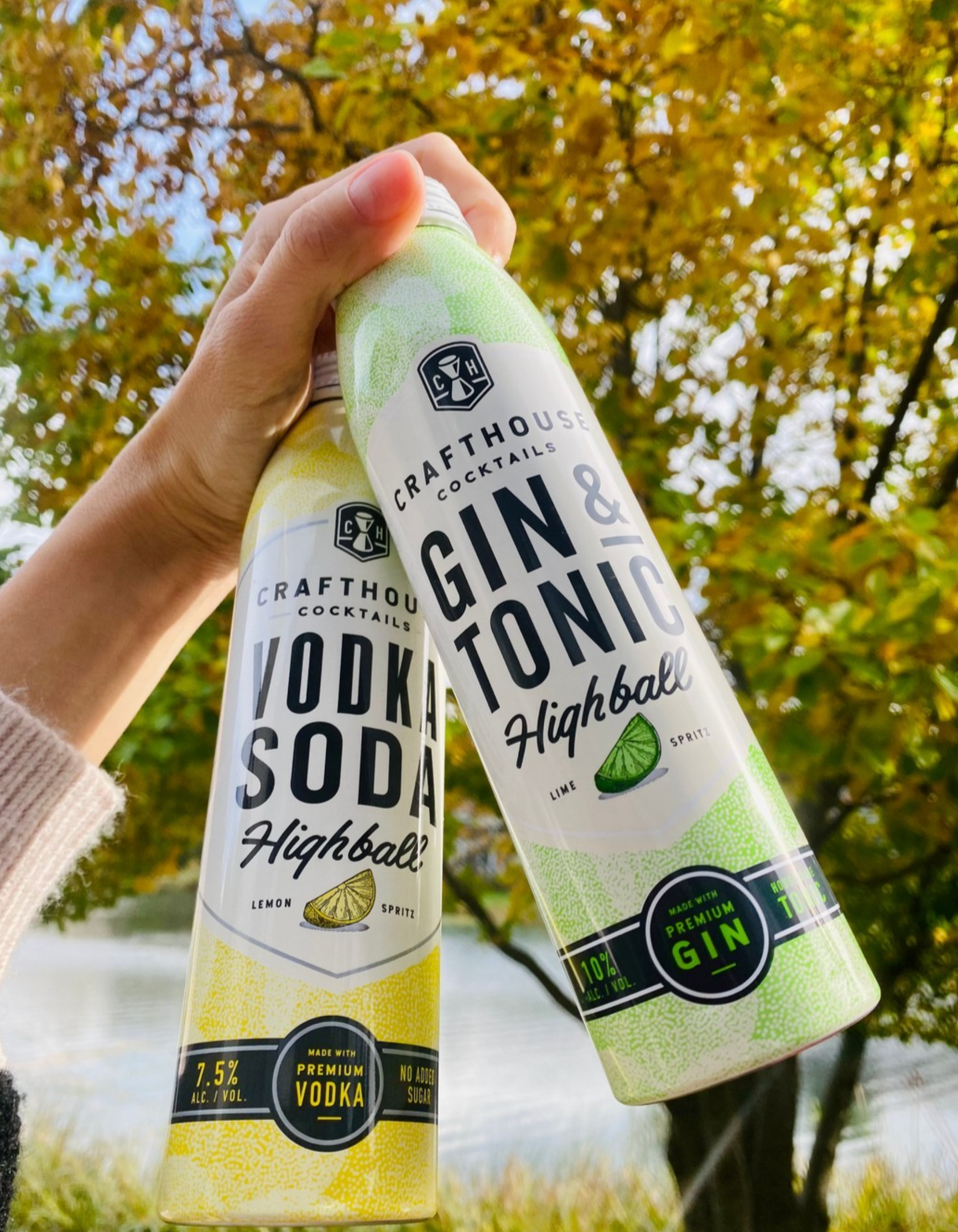 Hand holding Crafthouse Cocktails Gin and Tonic and Vodka Soda highball cans against autumn trees.