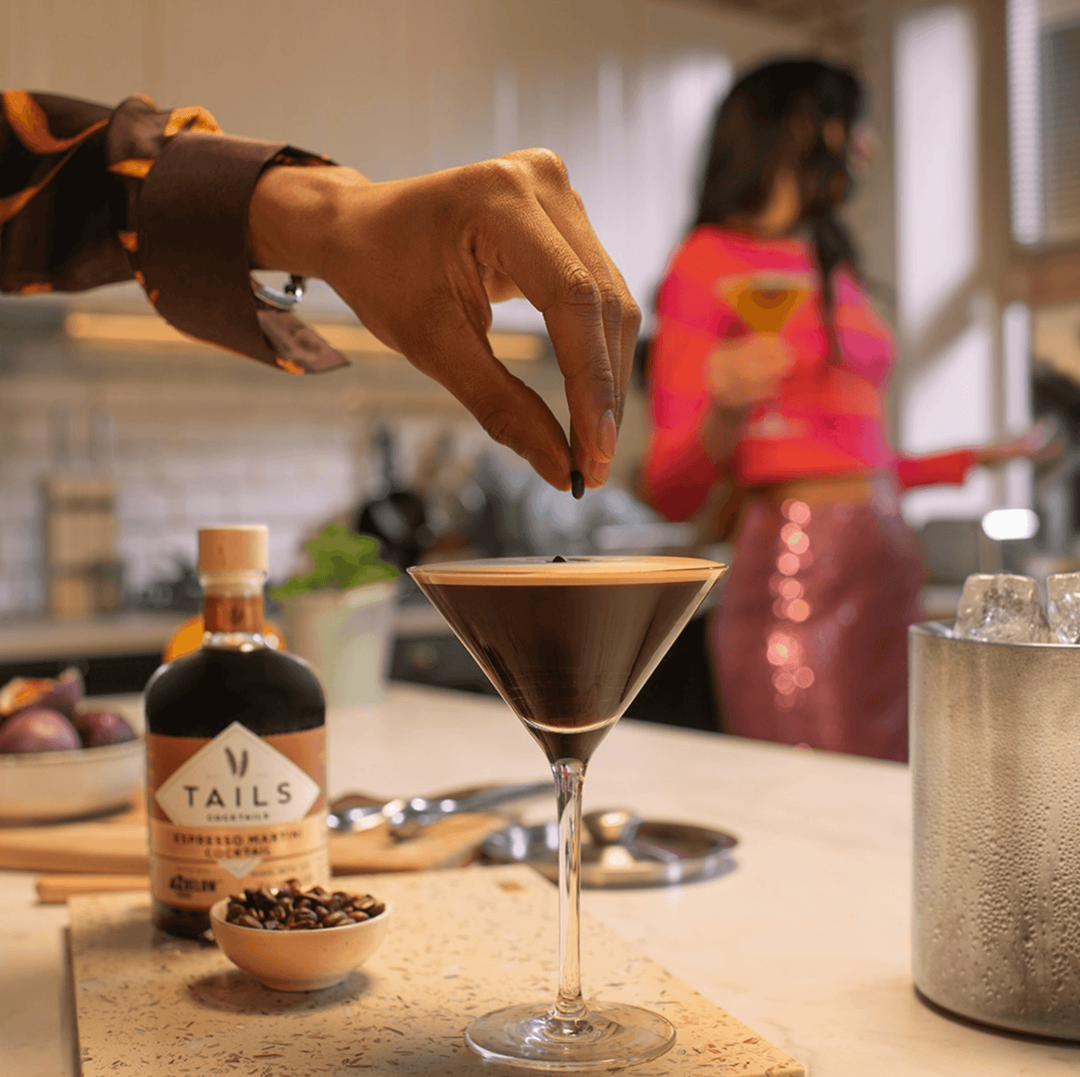Hand garnishing a Tails Espresso Martini with coffee beans in a stylish setting.
