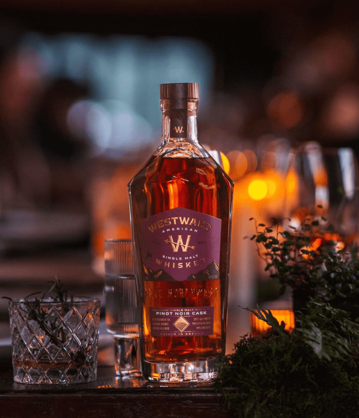 Westward American Single Malt Pinot Noir Cask Whiskey bottle on a table surrounded by candles and greenery.