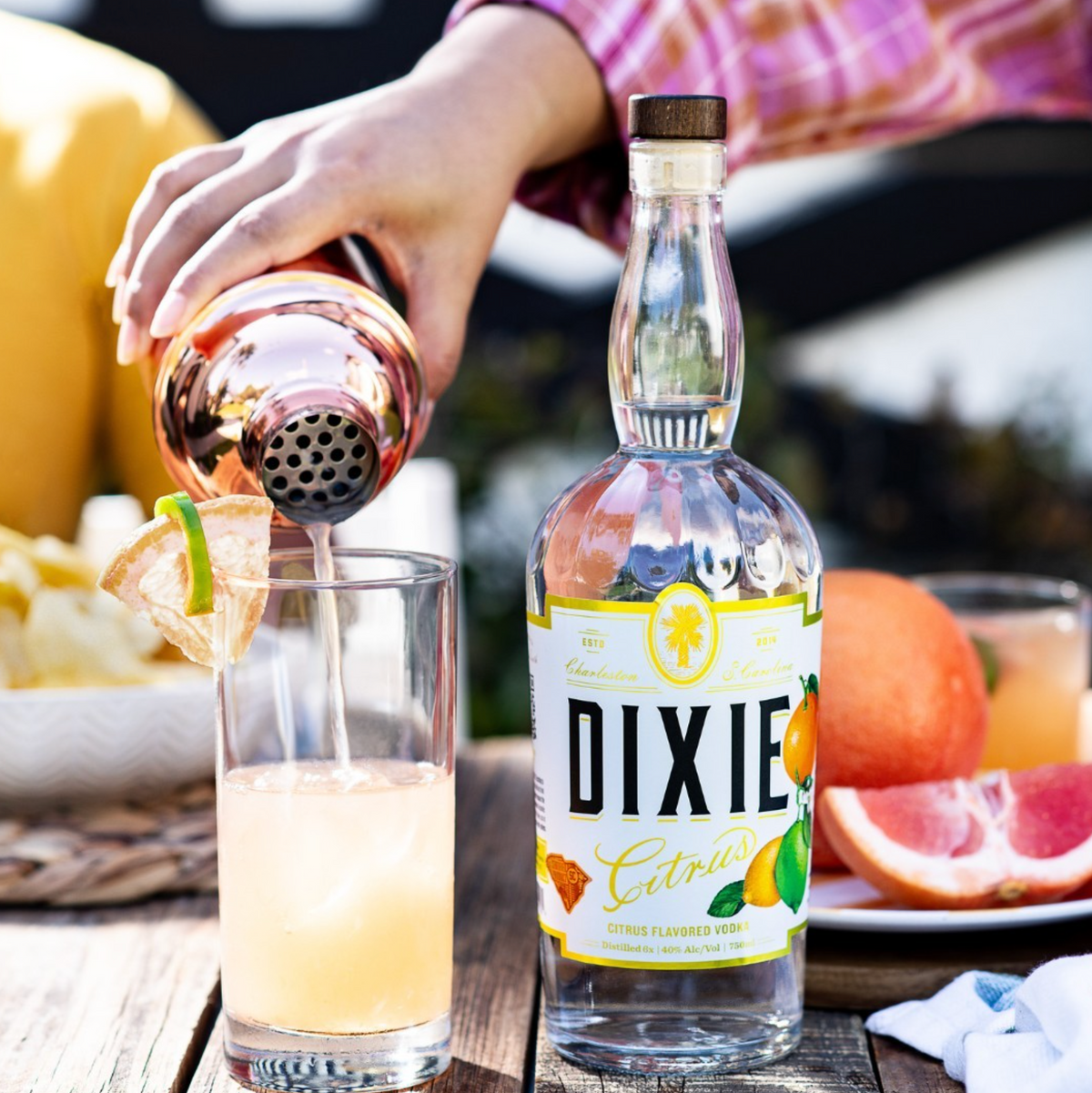 Pouring Dixie Citrus Flavored Vodka into a glass, surrounded by fresh Florida citrus and snacks.