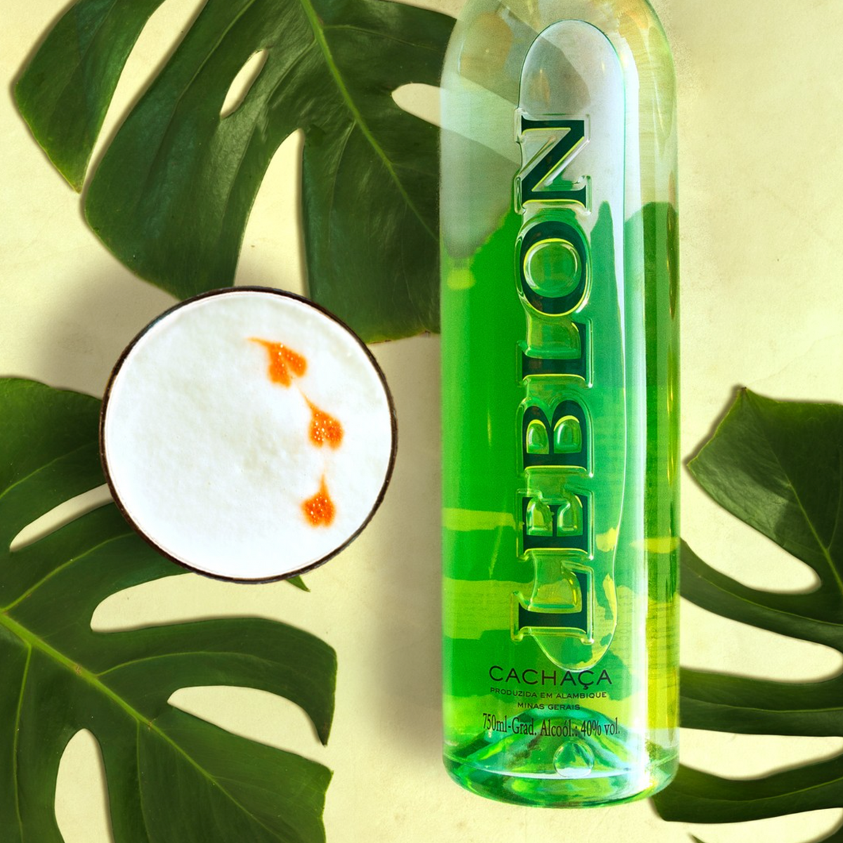 Bottle of Leblon Cachaça beside a cocktail, surrounded by green leaves.