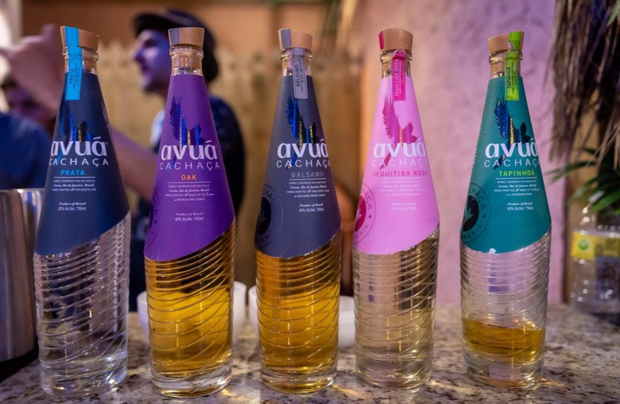 Five bottles of Avuá Cachaça showcasing various flavors including Oak and Prata on a countertop.