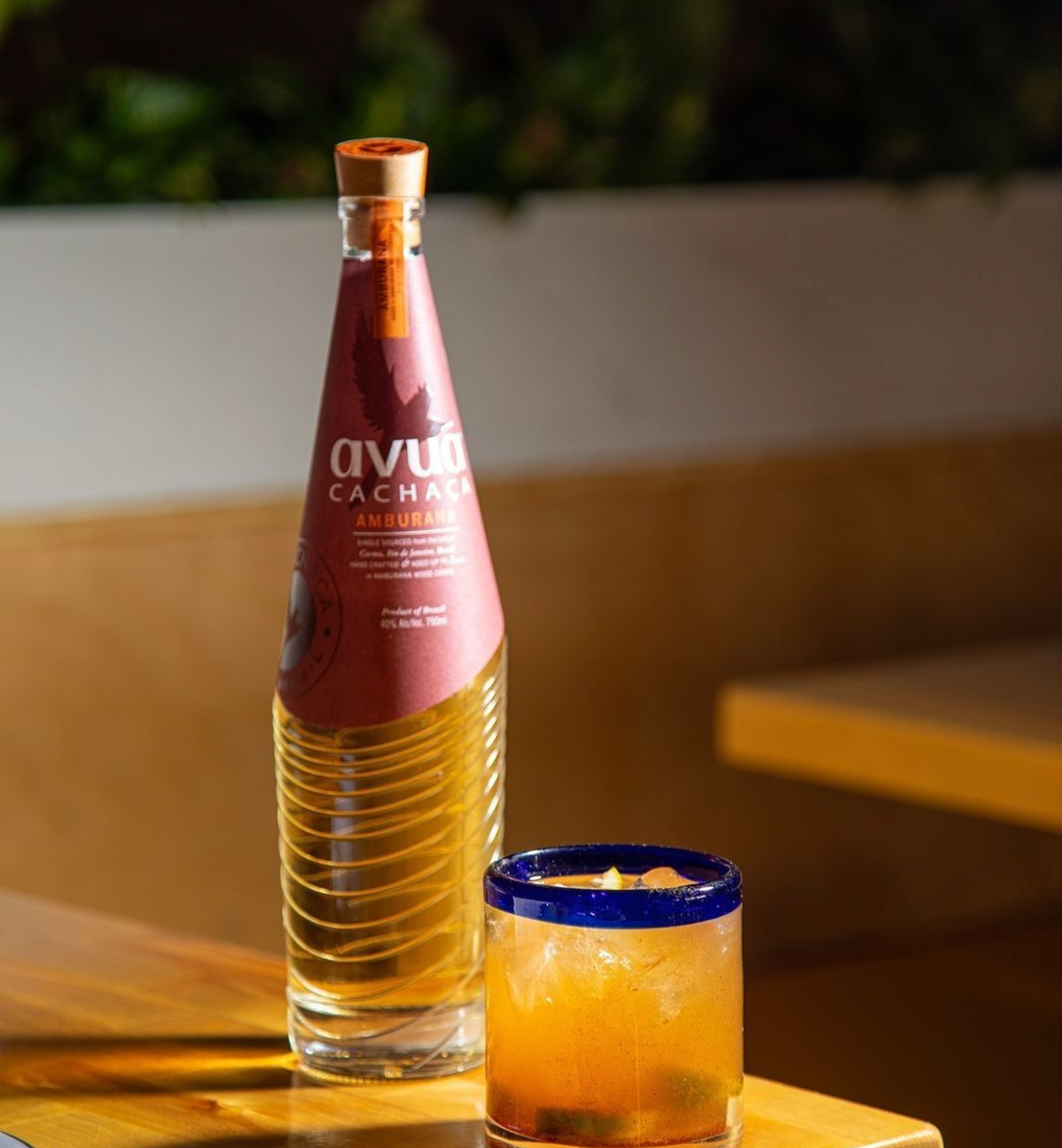 Bottle of Avuá Amburana Cachaça next to a cocktail in a glass, showcasing its unique flavor and artisanal quality.