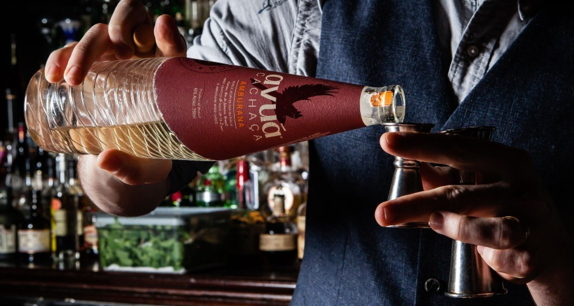 Bartender pouring Avuá Amburana Cachaça from a bottle into a jigger, showcasing unique cocktail craftsmanship.